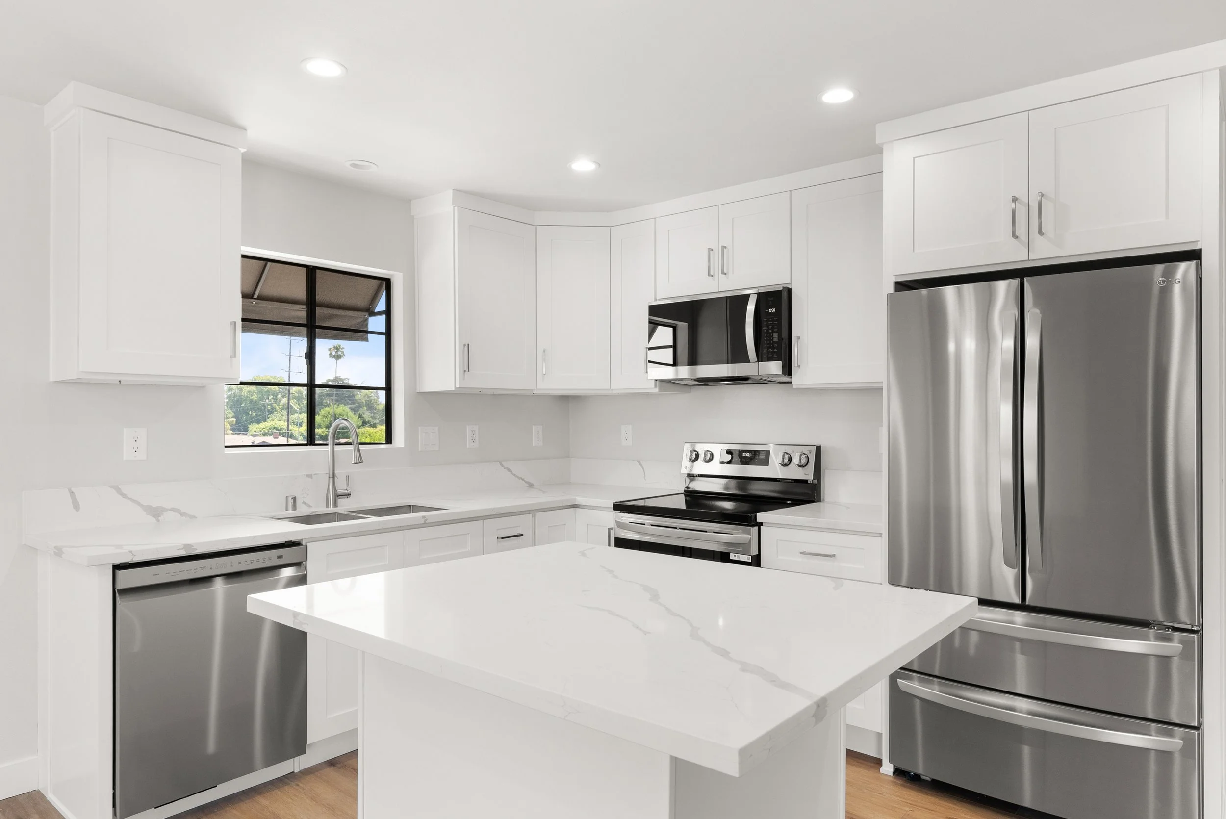 Modern kitchen with white cabinets, marble countertops, stainless steel appliances, and a large kitchen island.