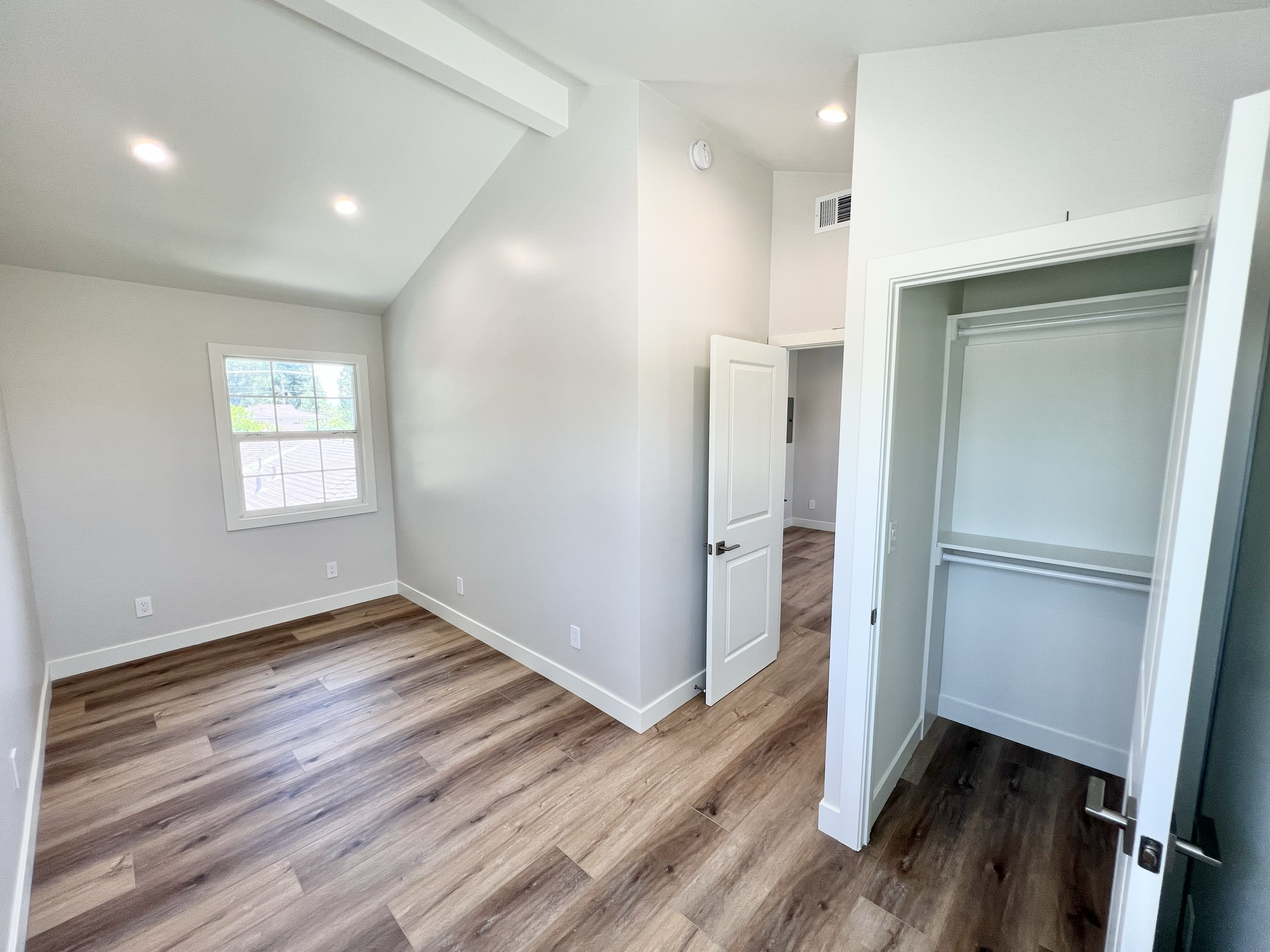 Empty room with wood flooring, a window, and an open closet.