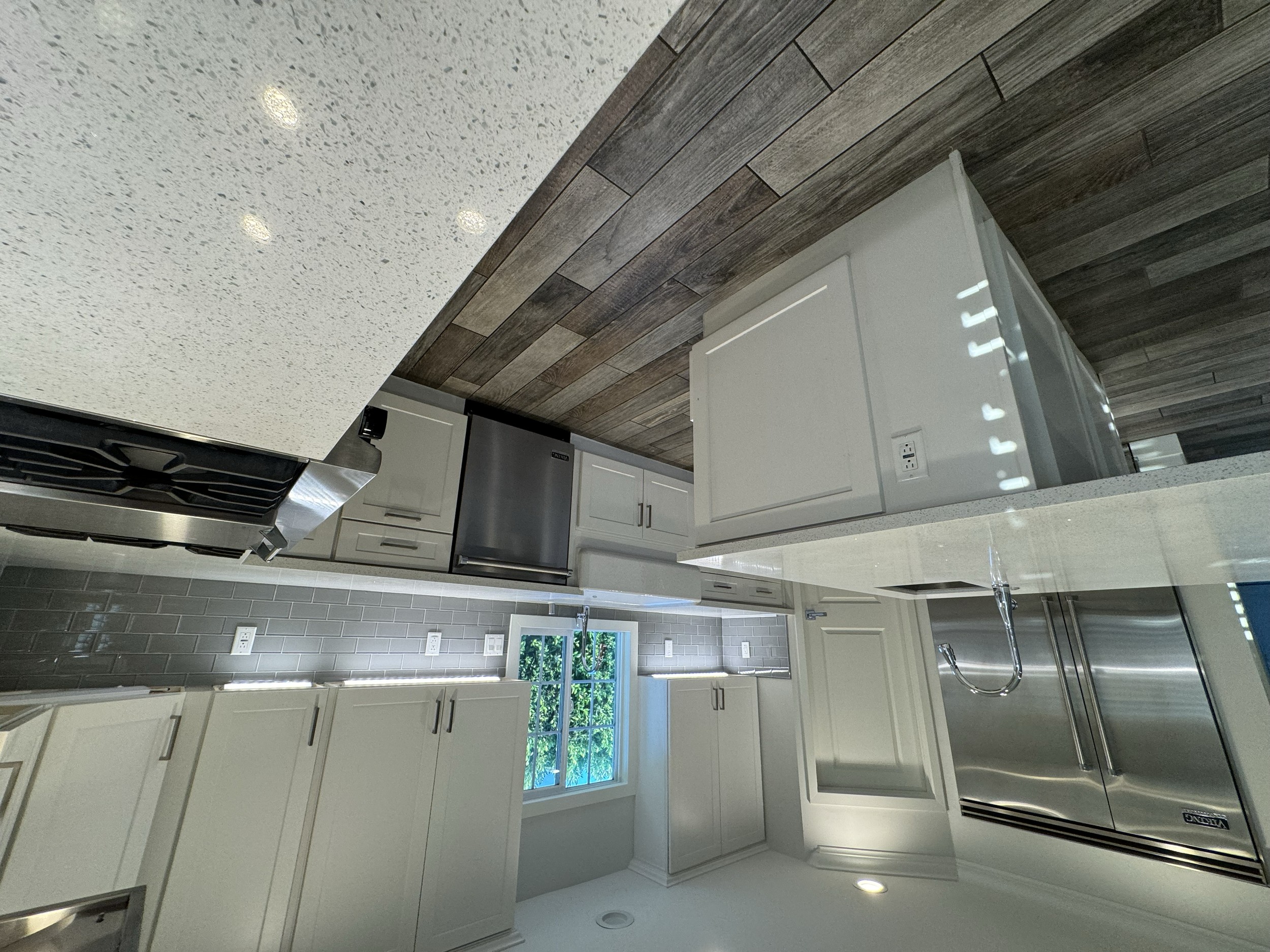 Modern kitchen with white cabinets, stainless steel appliances, gray tiled backsplash, and a window overlooking greenery.