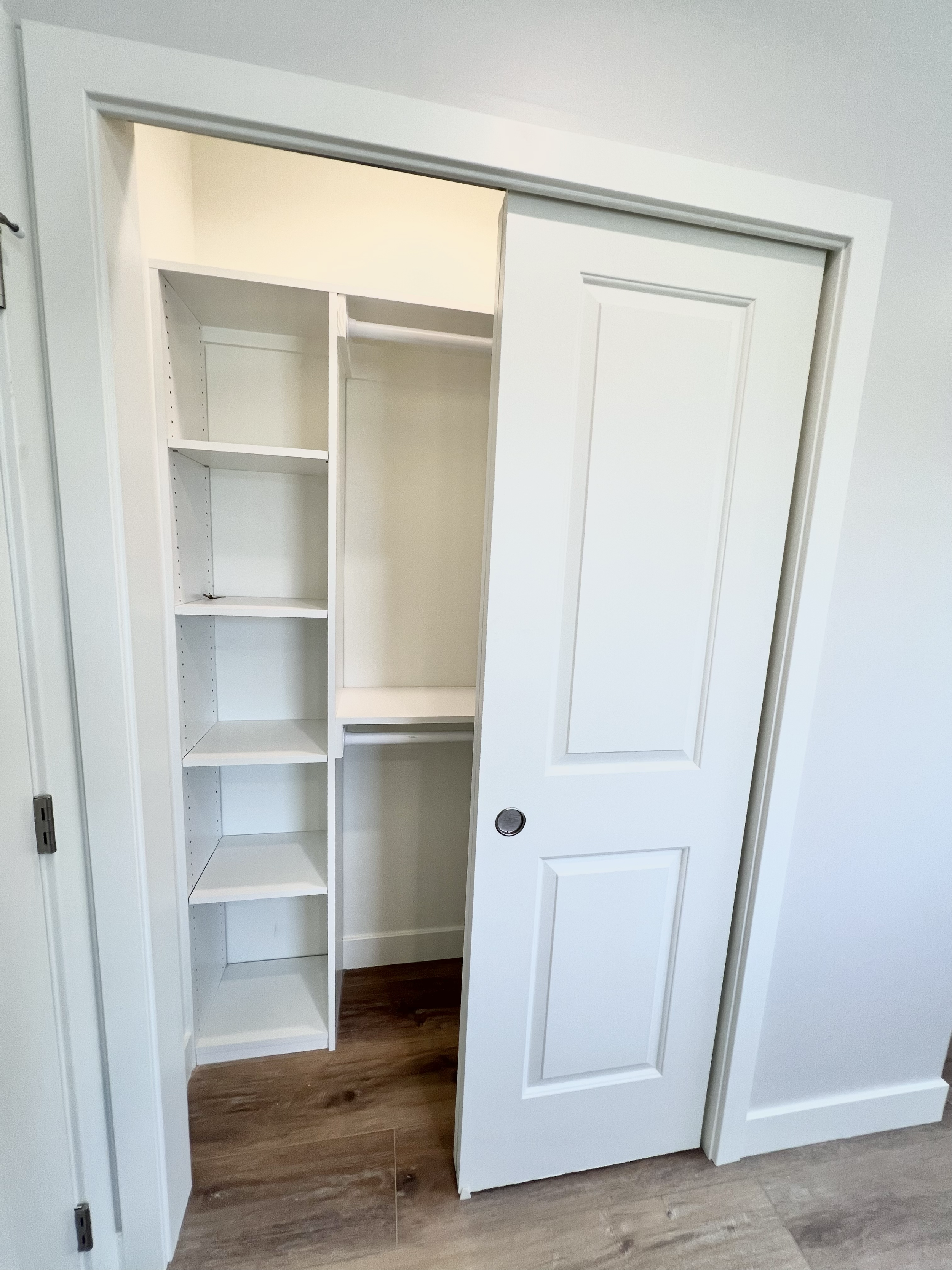 Empty white closet with sliding door, shelves on the left, and a rod for hanging clothes inside.