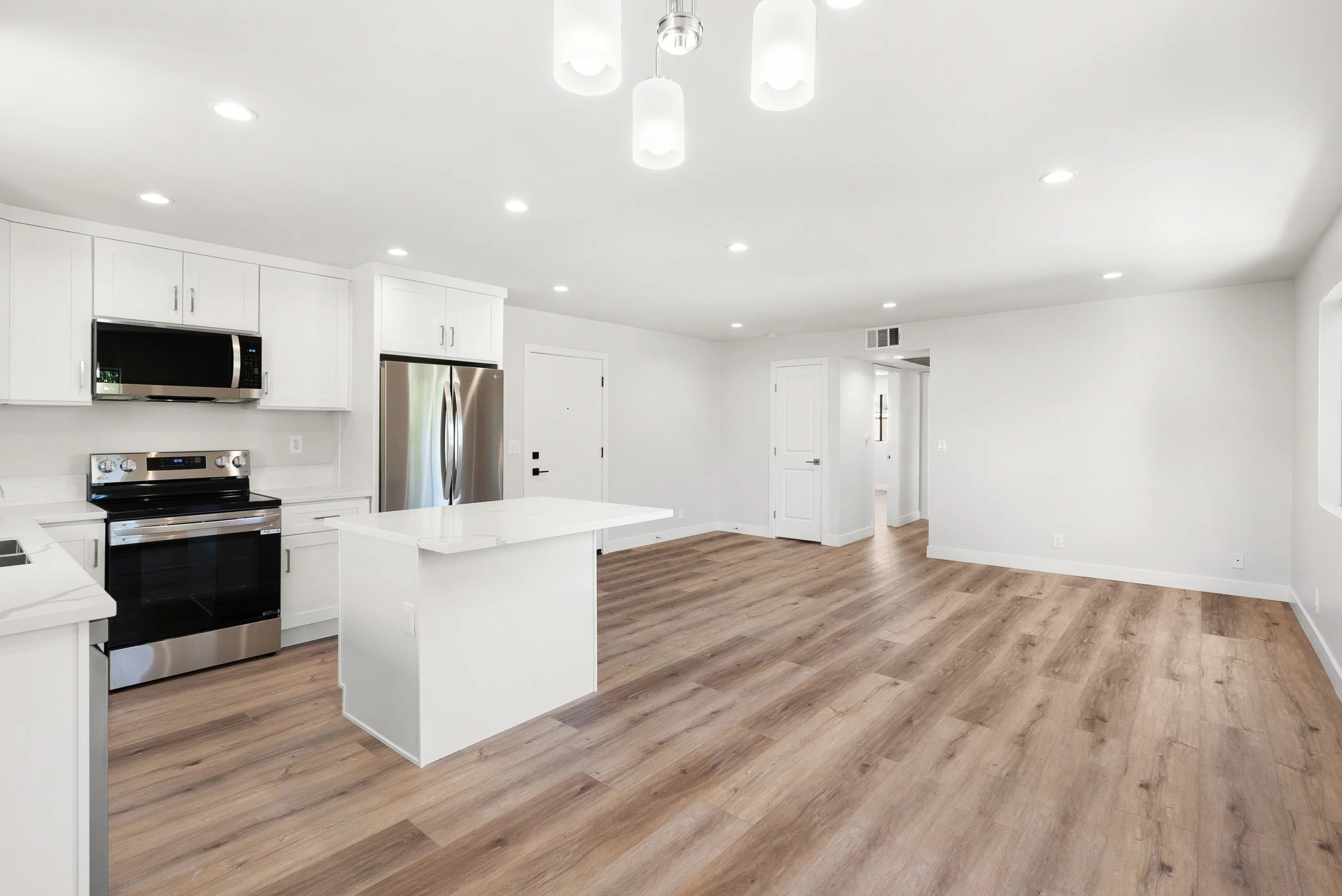 Empty modern kitchen and dining area with white cabinets, stainless steel appliances, and wood flooring.