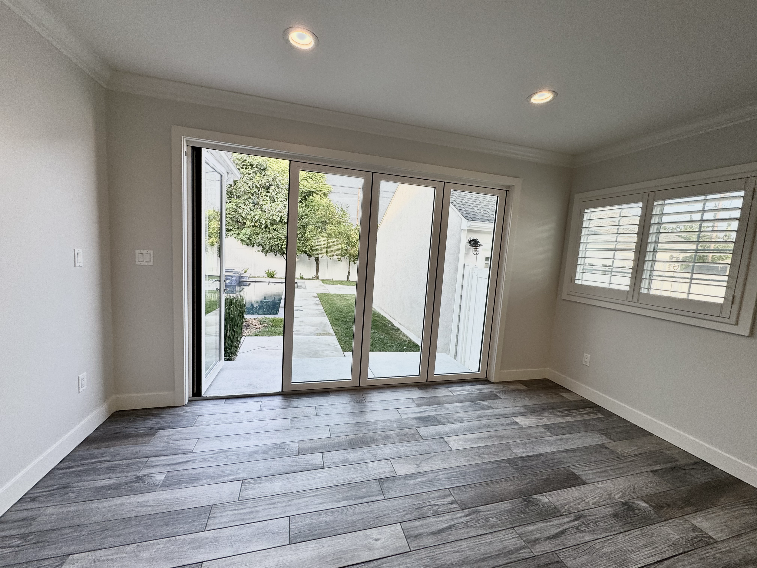 Empty room with sliding glass door leading outside, and window with shutters, hardwood floor, and ceiling lights.