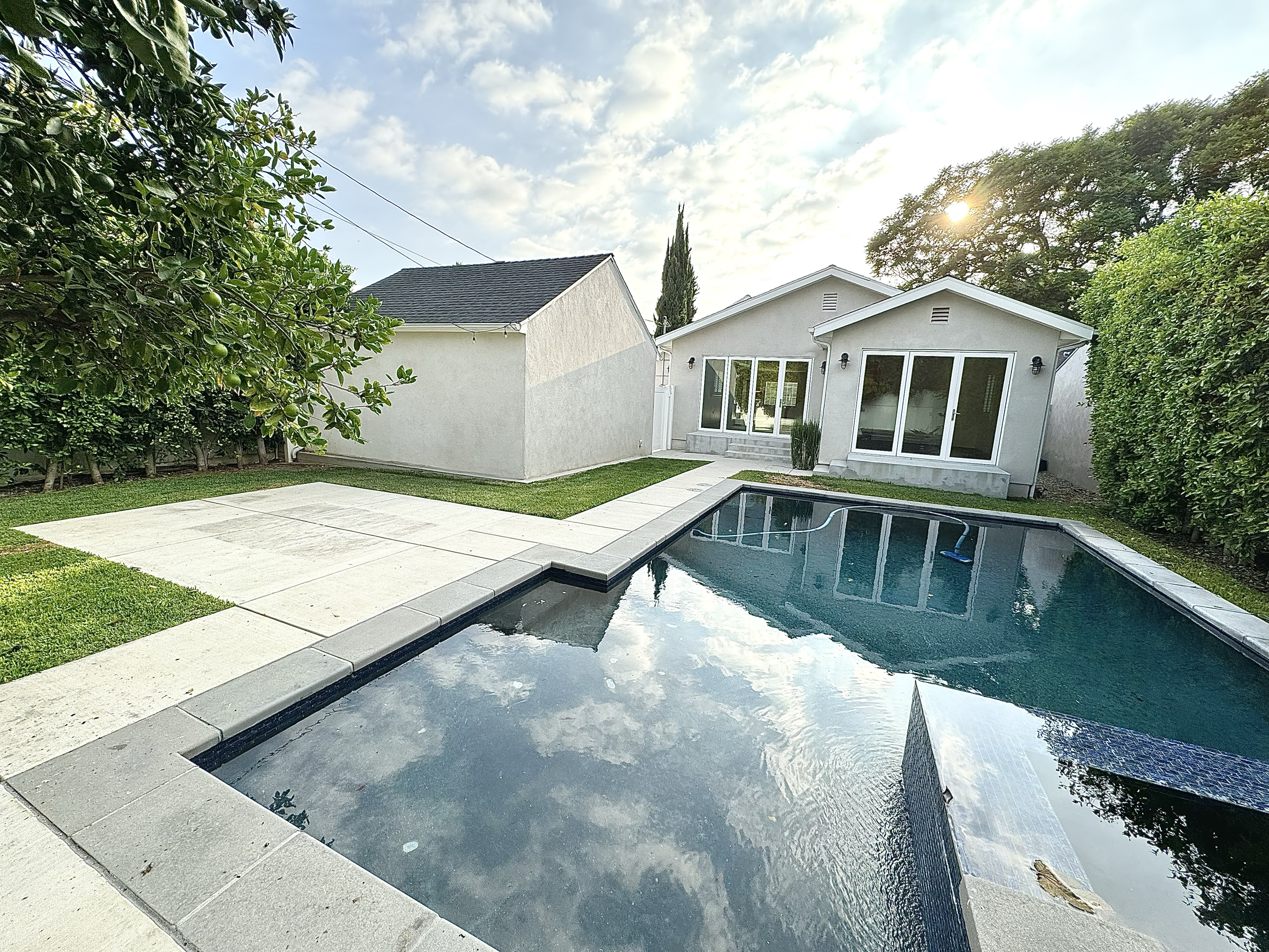 Backyard with swimming pool, white house, green trees, and cloudy sky.