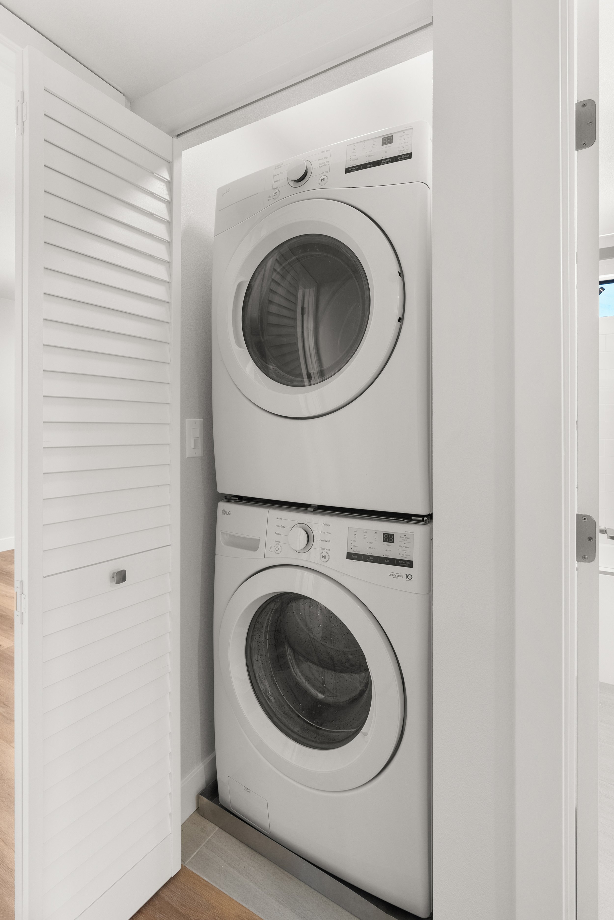Stacked white front-loading washer and dryer inside a closet with an open louvered door.