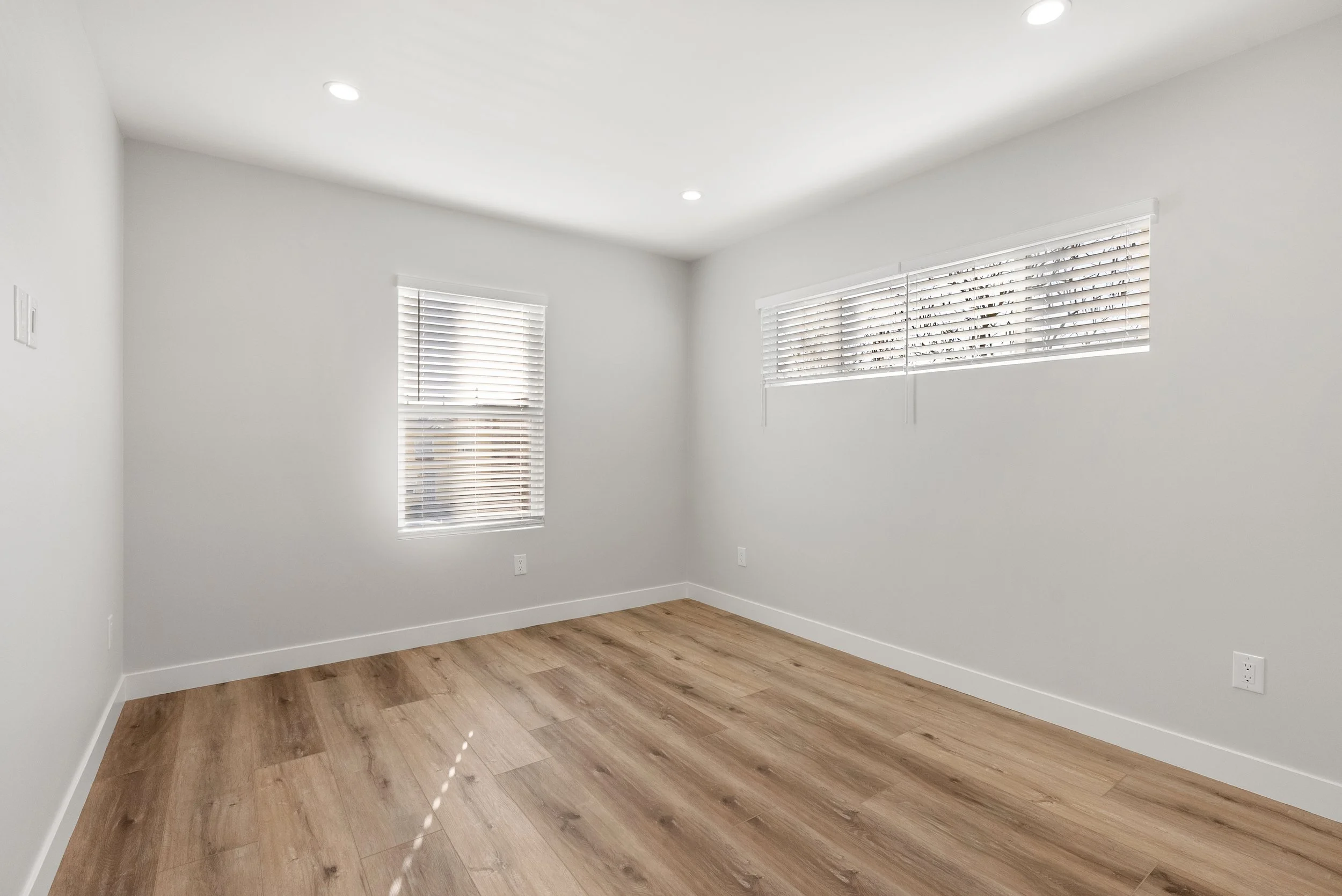 Empty room with white walls, wooden floor, and three windows with white blinds.