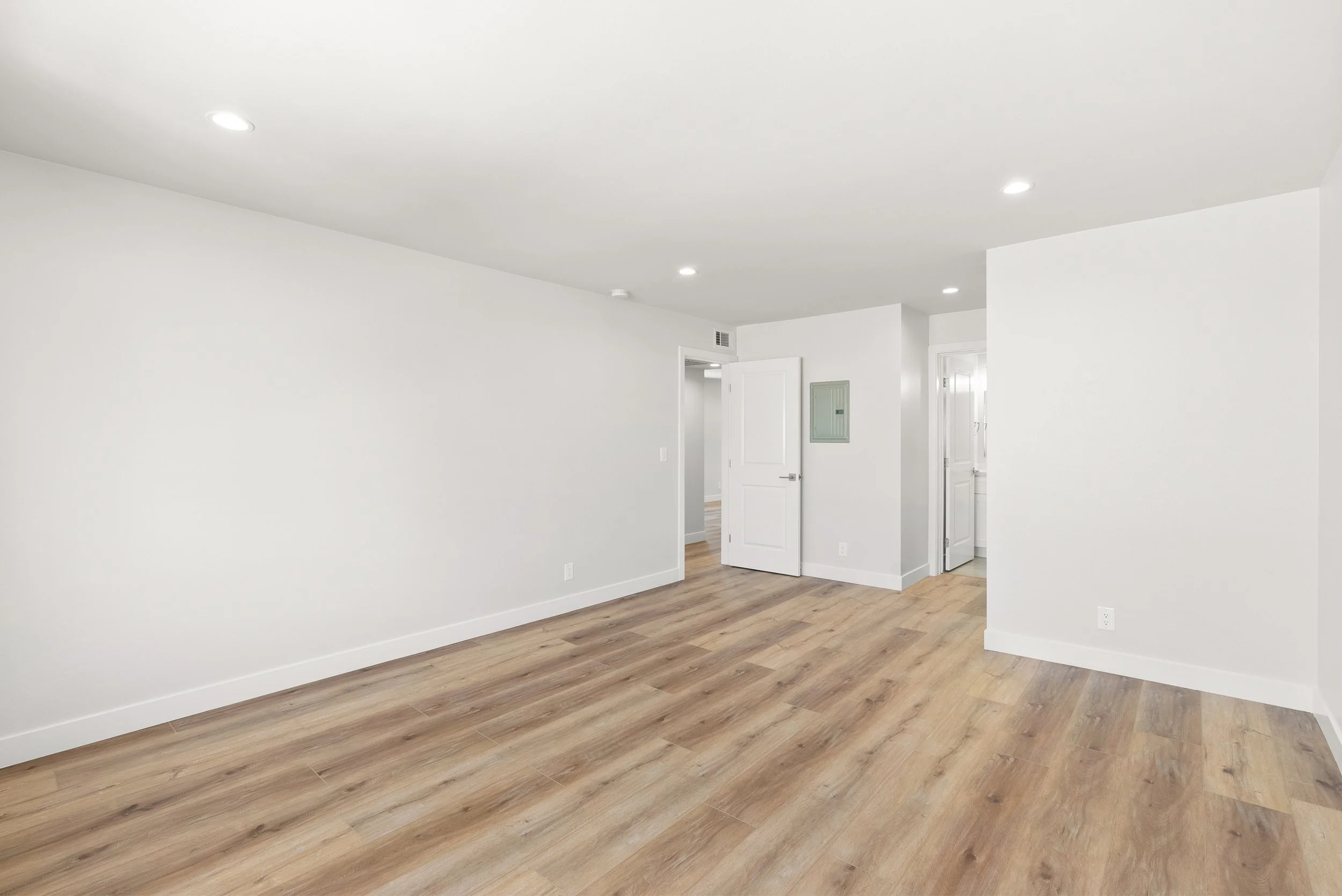 Empty room with white walls, wood flooring, and open doors.