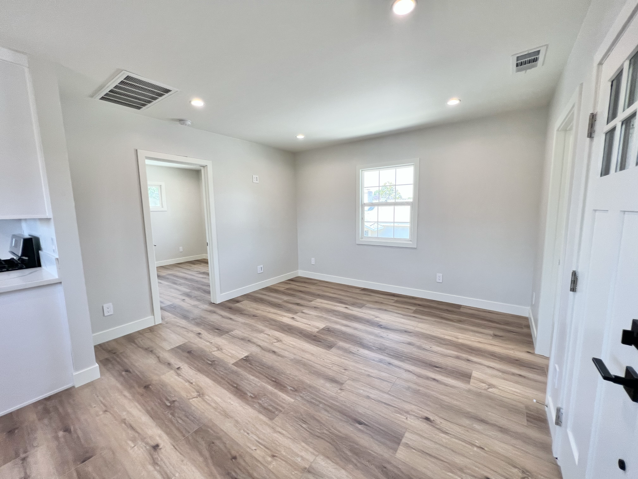 Empty living room with white walls, a window, and wood flooring.