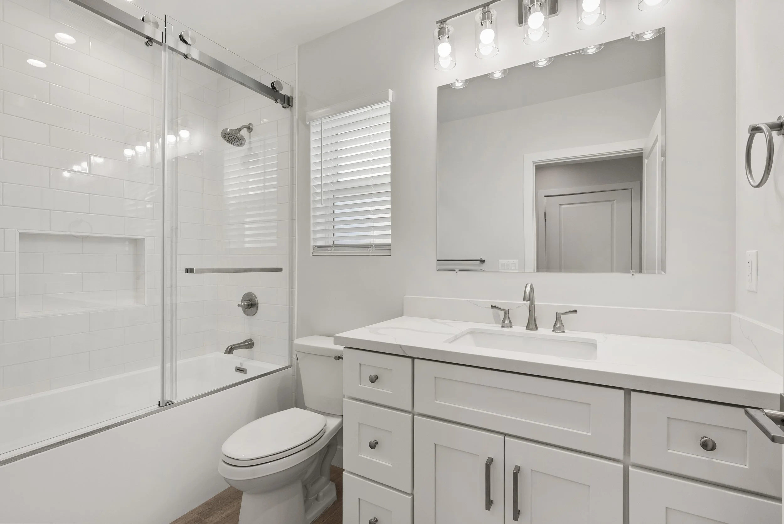 Modern bathroom with white vanity, marble countertop, large mirror, toilet, and glass-enclosed shower with white subway tiles.