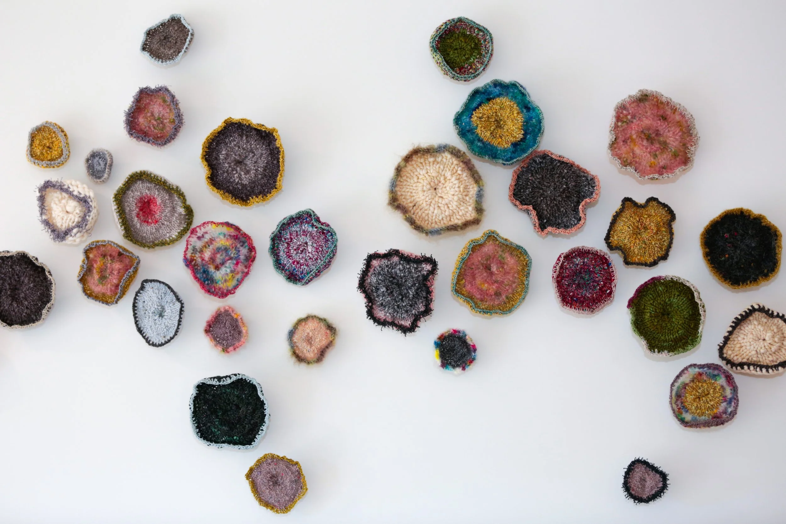 Colorful, knitted or crocheted circle pieces scattered on a white background.