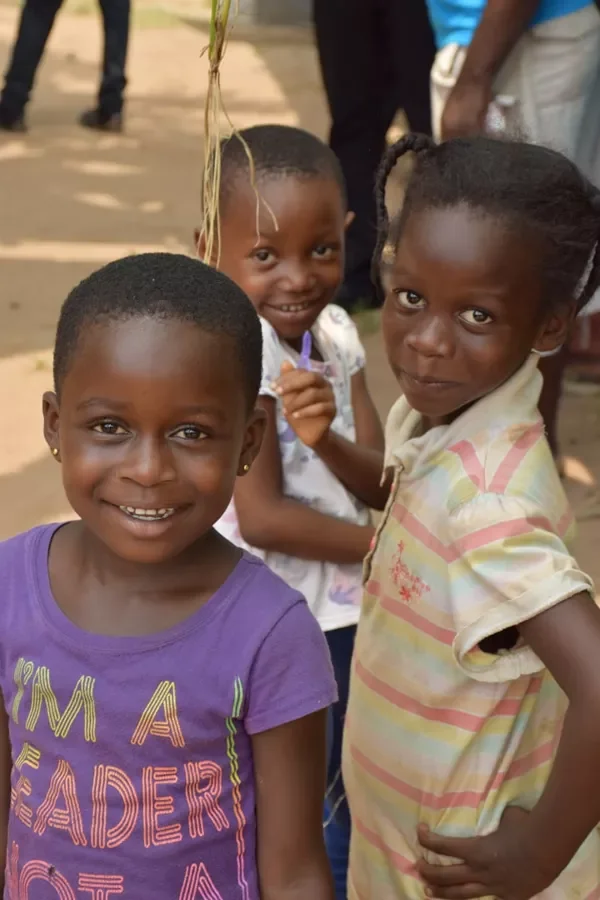 Three young girls smiling outdoors, with two in the foreground and one slightly behind, in a casual setting.