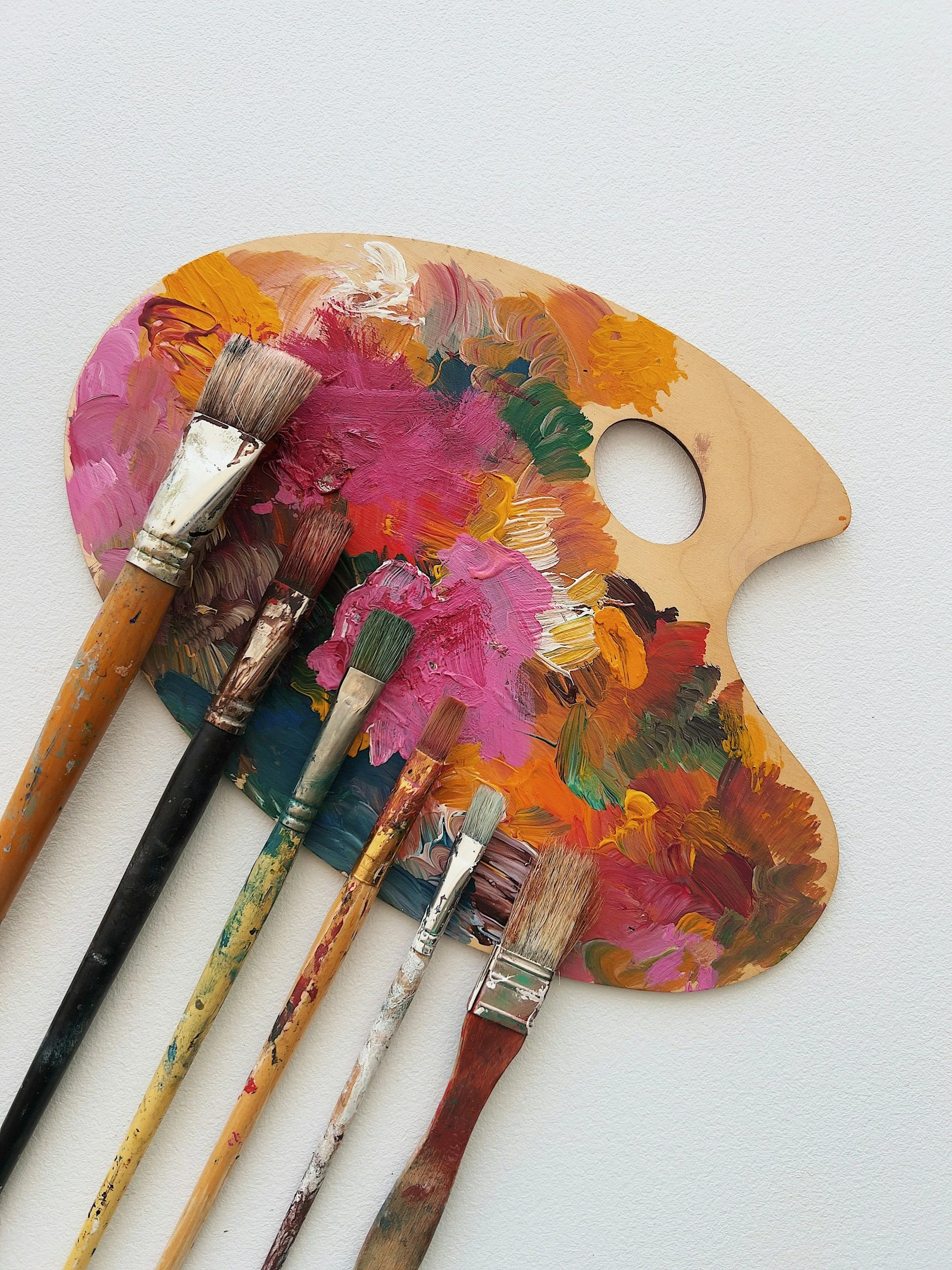 Wooden artist's palette with colorful paint and several paintbrushes resting on it.