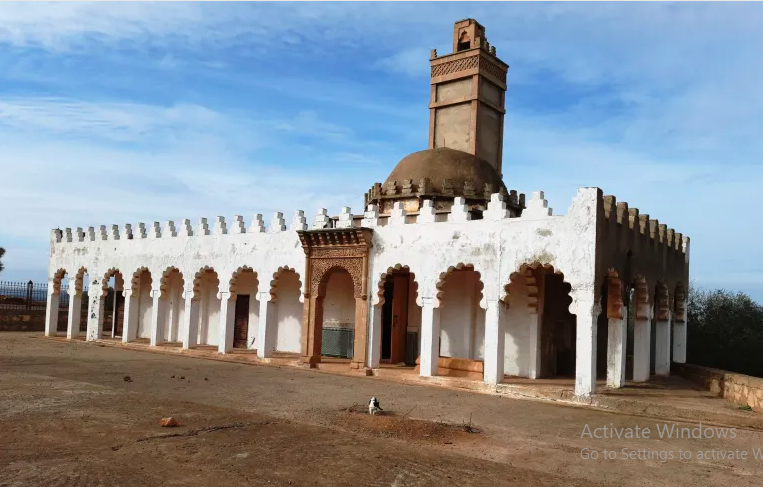 Shrine of ʿAbd Allāh ibn Yāsīn al-Jazūlī (Romani, near Rabat) — A whitewashed shrine with arches, a dome, and a tall minaret, rising quietly over an open rural landscape.
