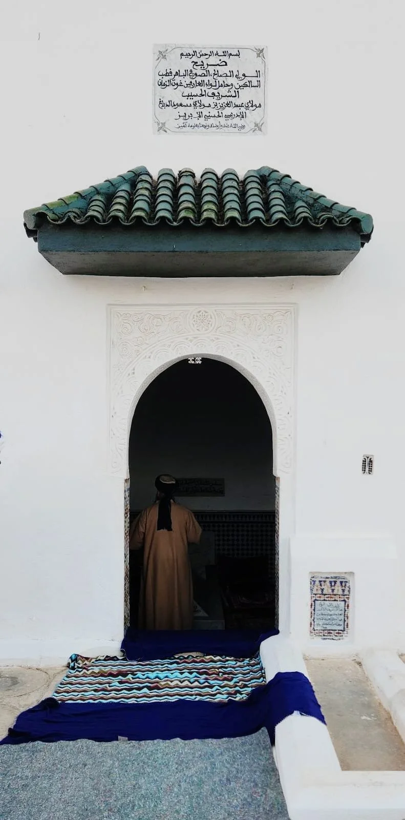 man in traditional Moroccan dress stands at the arched doorway of the rawḍa of Mawlāy ʿAbd al-ʿAzīz al-Dabbāgh, Fez.