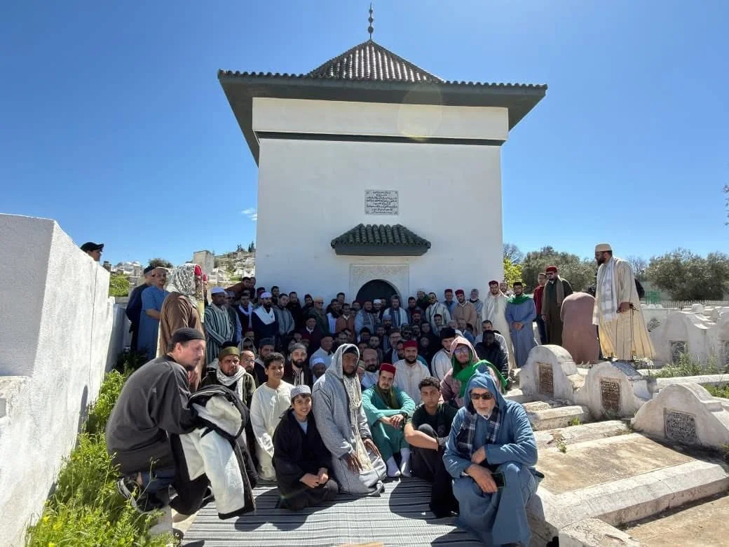 A large group of men gathered for a spiritual heritage tour in front of the whitewashed qubba of Mawlāy ʿAbd al-ʿAzīz al-Dabbāgh outside Bāb al-Futūḥ, Fez, Morocco.