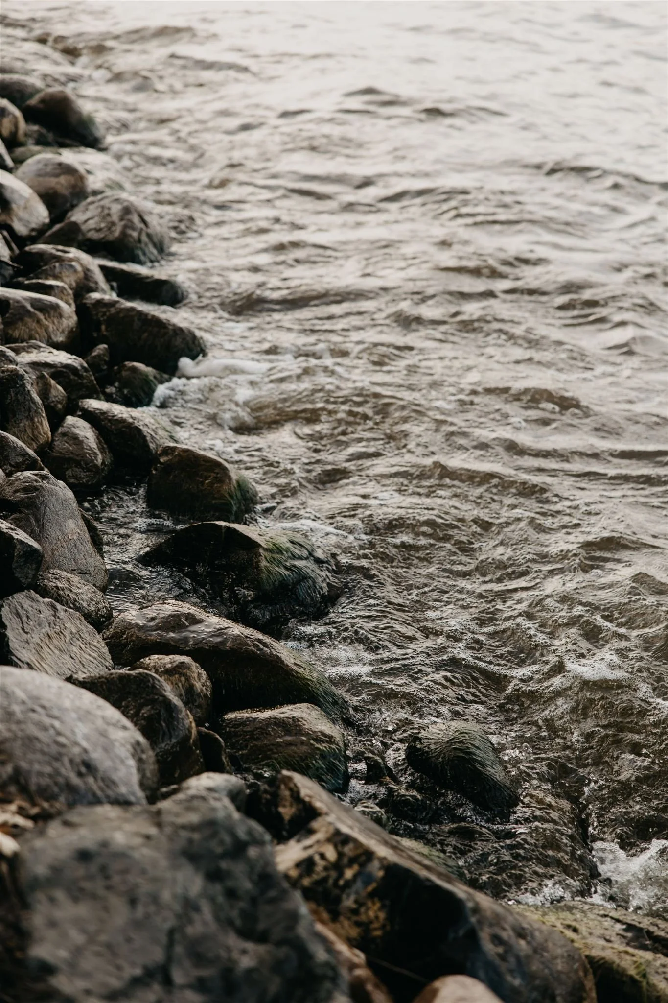 Photo of rocky shoreline next to a body of water with gentle waves.