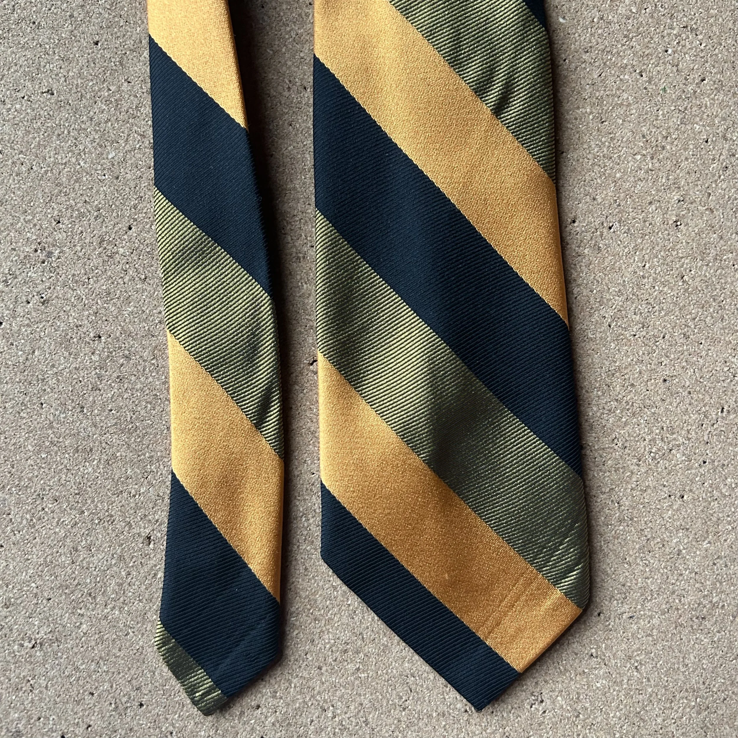 A necktie with diagonal stripes in colors including gold, dark blue, and green, laid flat on a textured beige surface.