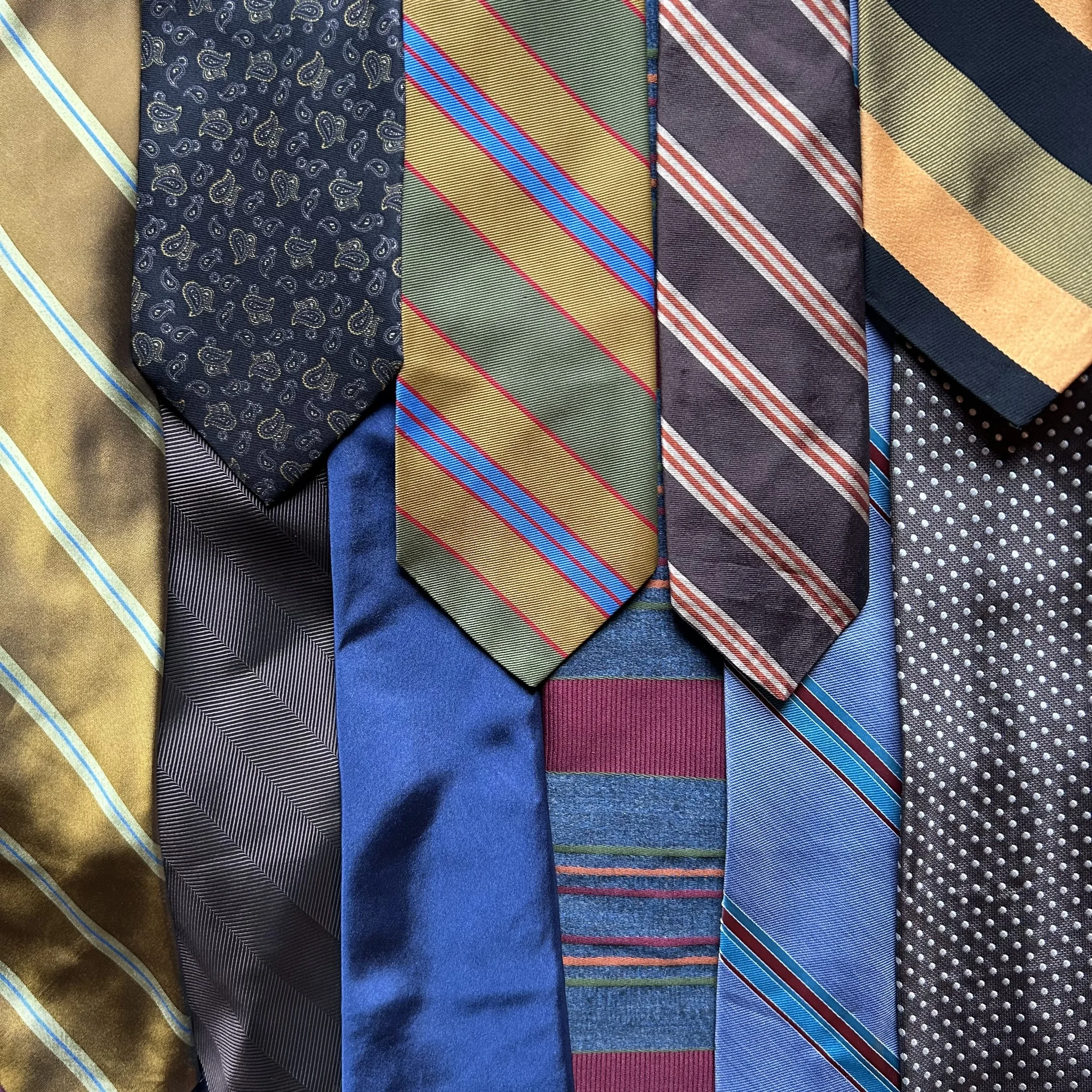 Multiple men's neckties with various colors and patterns, including stripes, polka dots, paisley, and solids, arranged in a row.