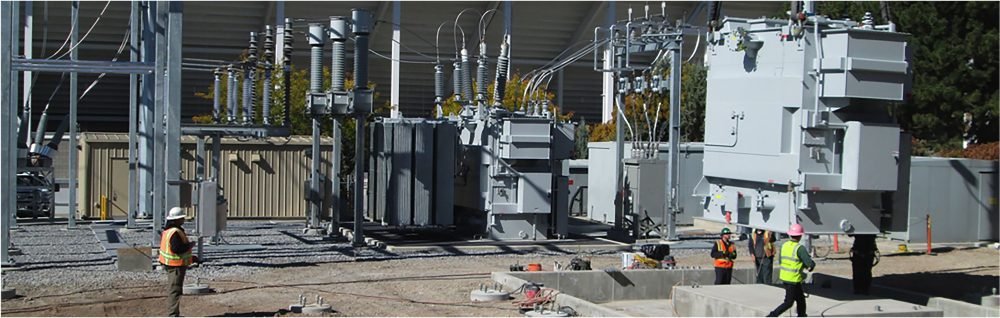Construction workers at a power substation installing electrical transformers.