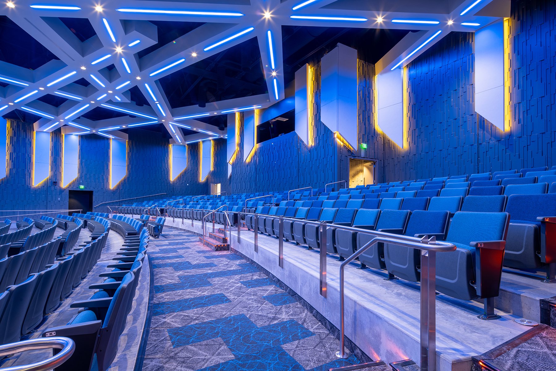 Union Middle School's auditorium features a star-pattern LED ceiling grid above tiered blue seating and amber-lit wood slat walls.