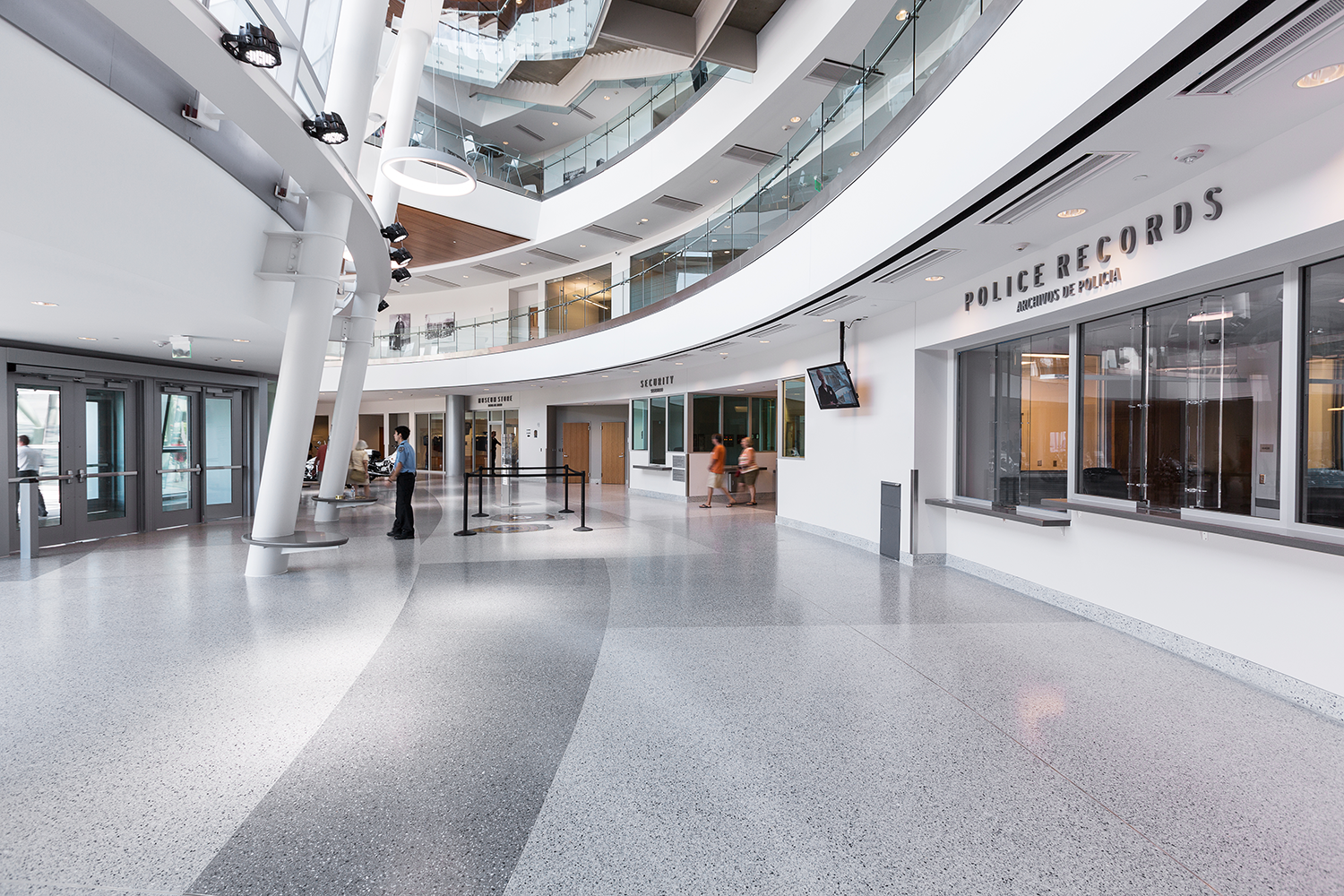 Interior of a modern building lobby with multiple floors, a security desk, police records office, glass railings, and a few people walking inside.
