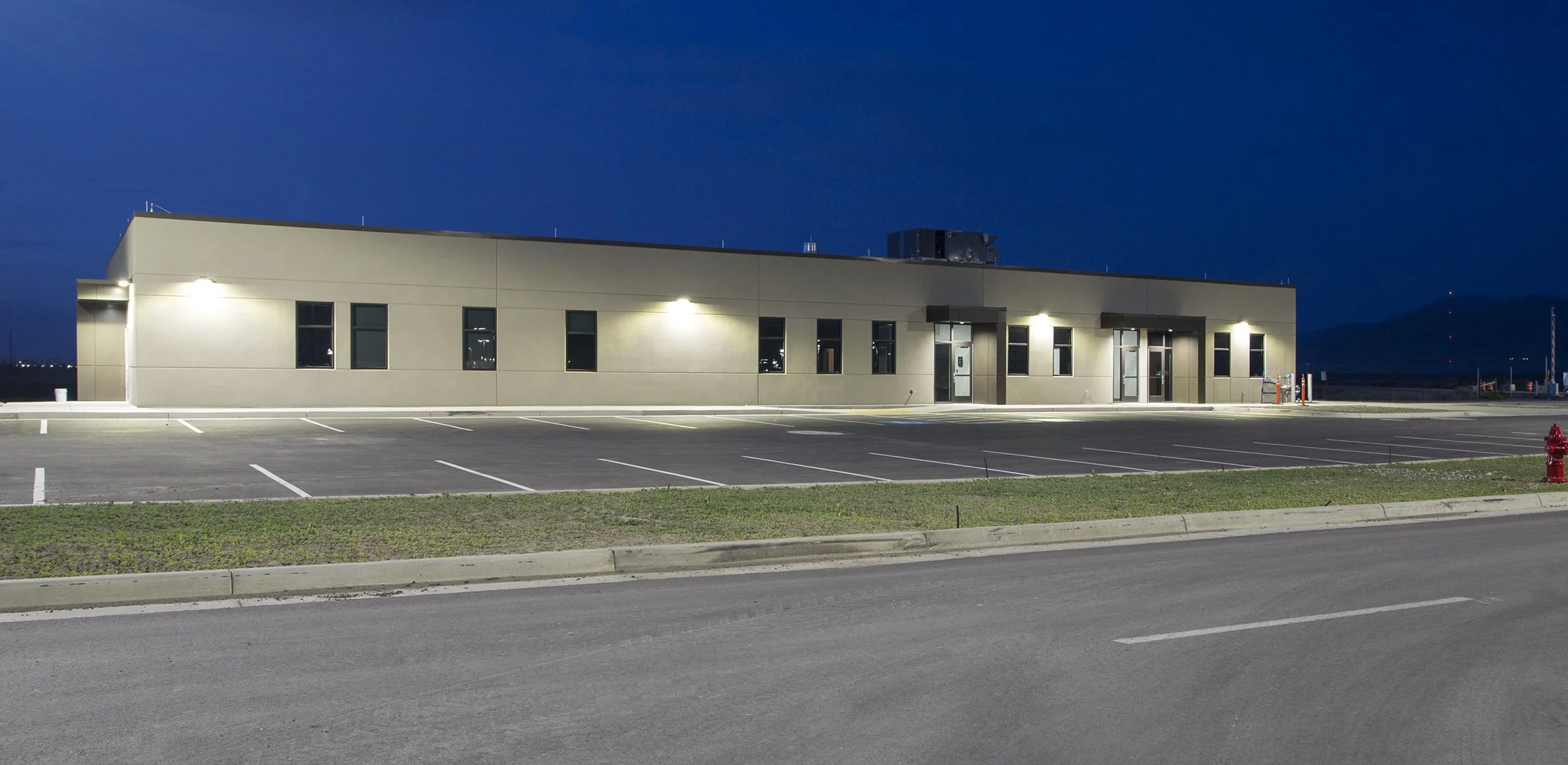 Empty parking lot with a commercial building illuminated at night, with a mountain in the background.