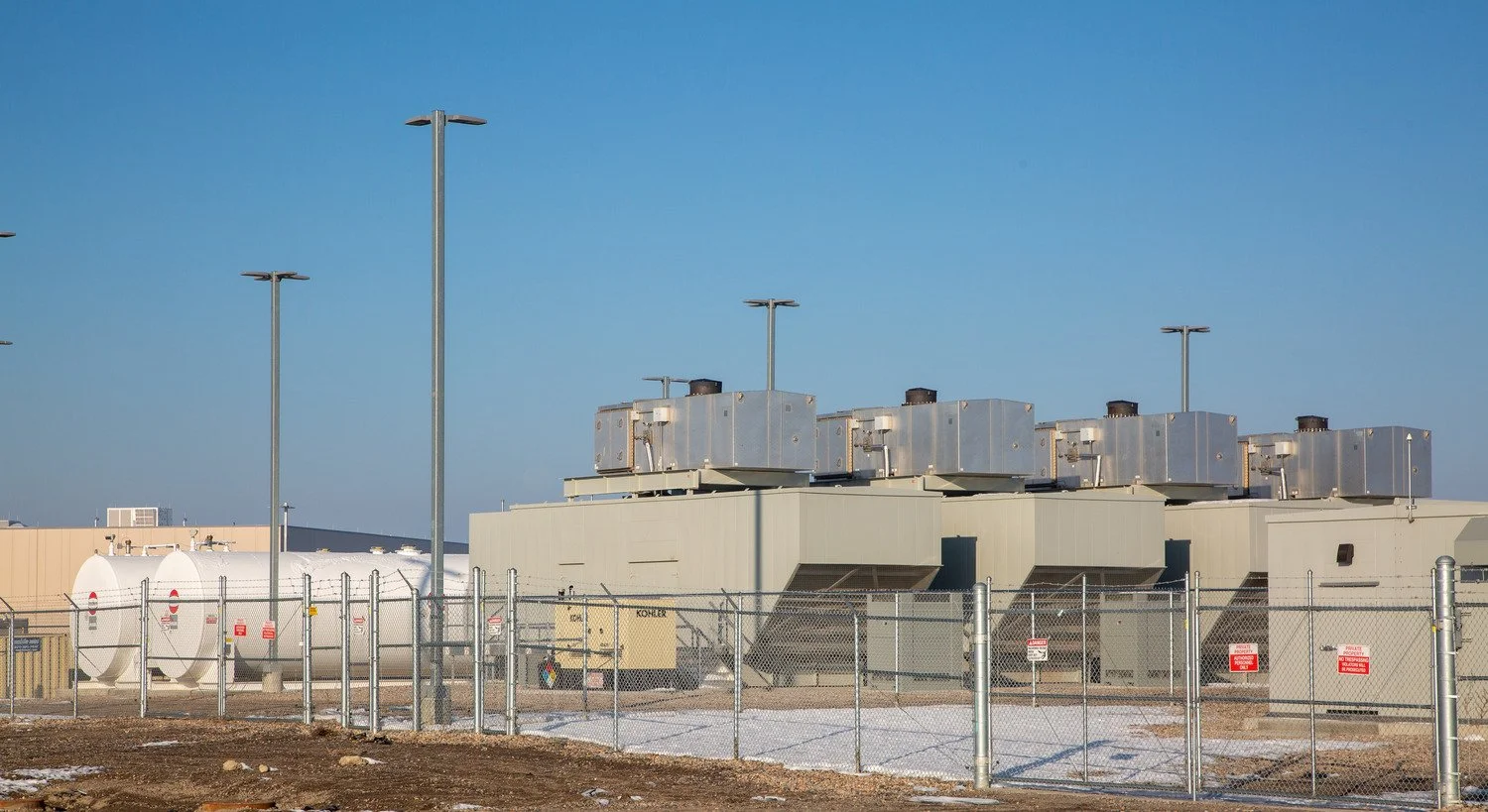 Standby generators and fuel storage tanks in a fenced backup power yard.