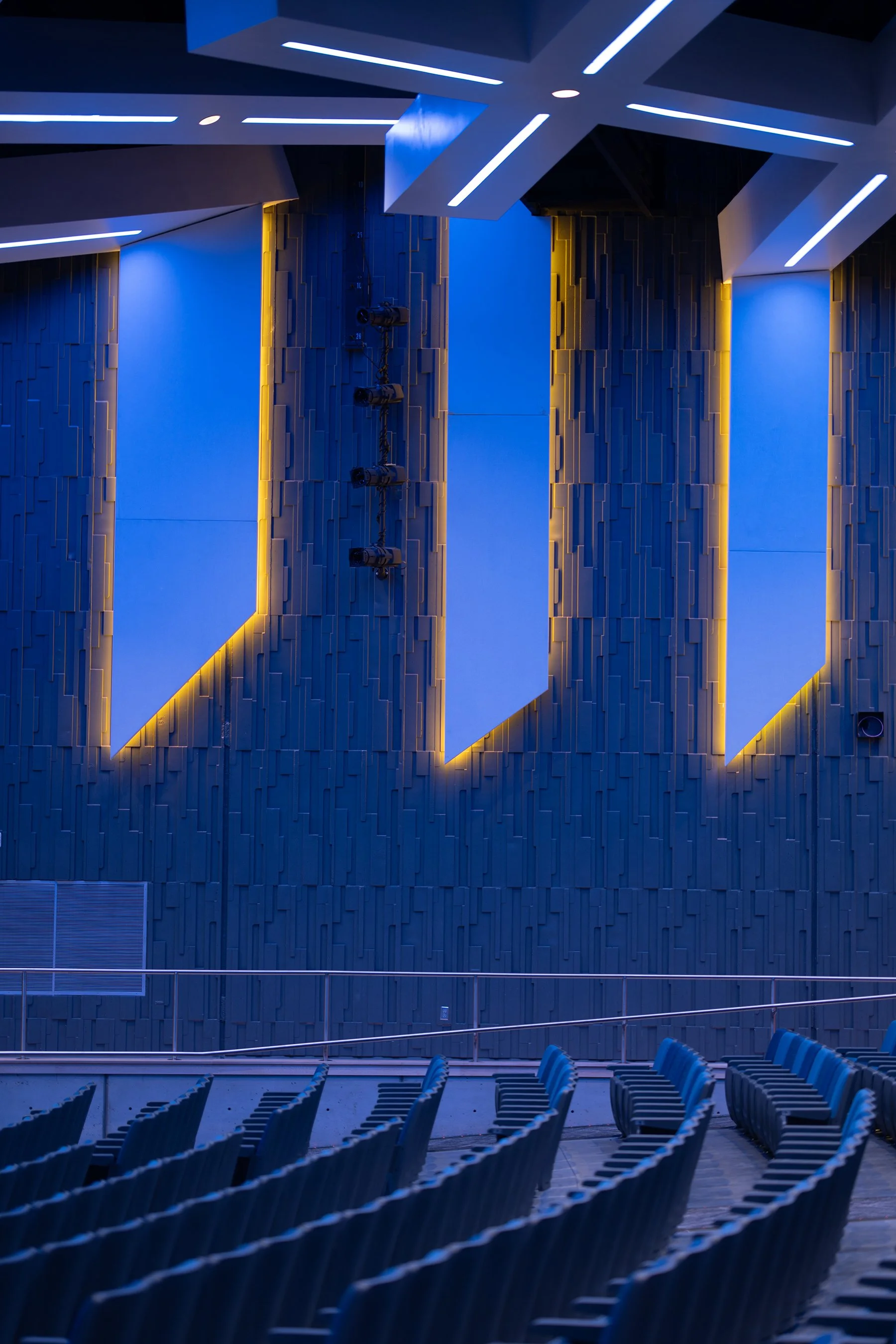 Amber-lit vertical accents in Union Middle School's auditorium wall rise above rows of blue theater seating.