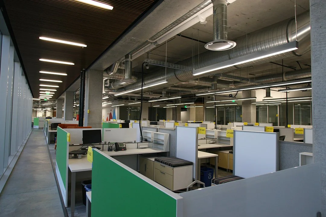 Empty modern office with cubicles, computers, and industrial ceiling pipes.