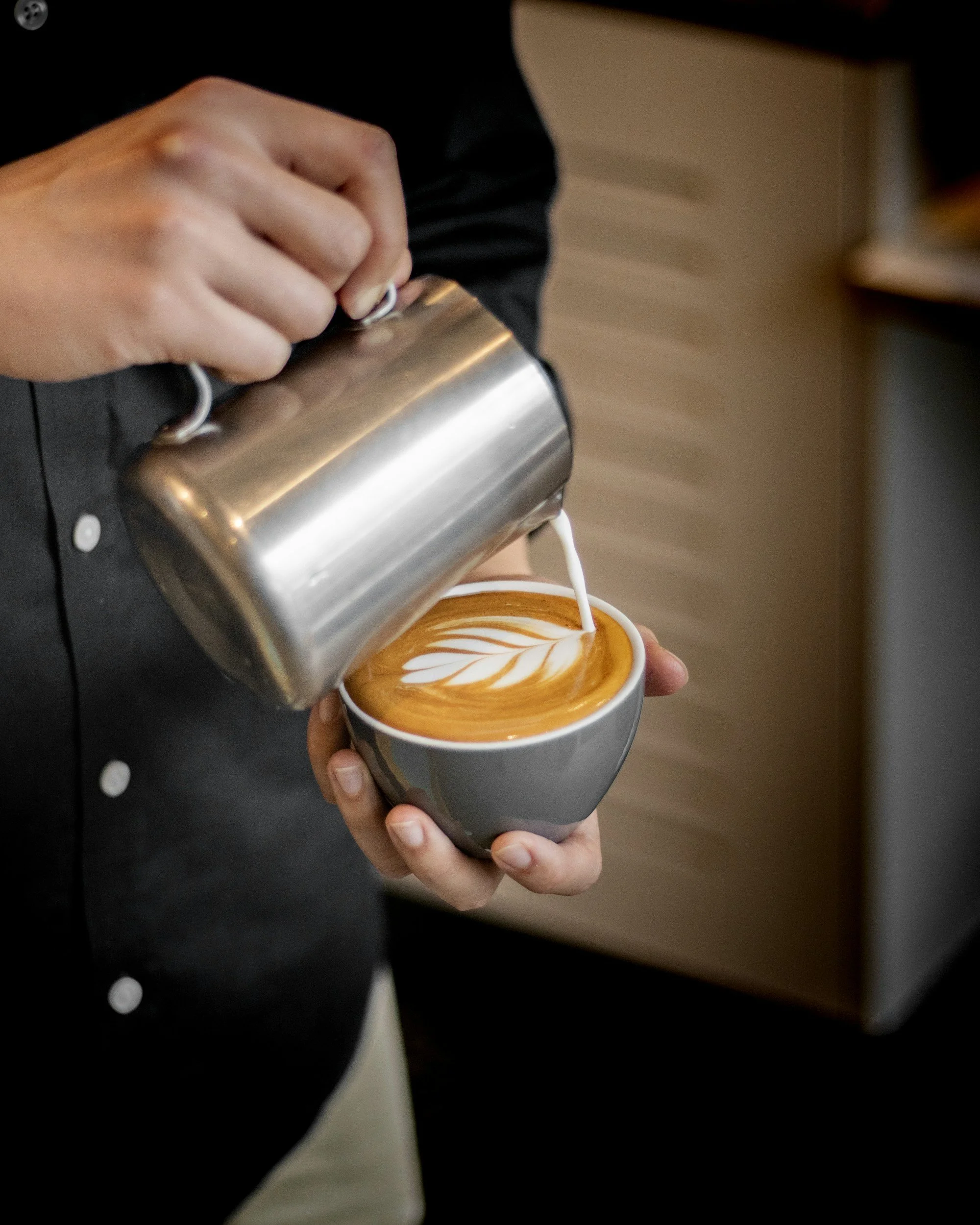 Barista pouring steamed milk into a cup of espresso to create latte art.