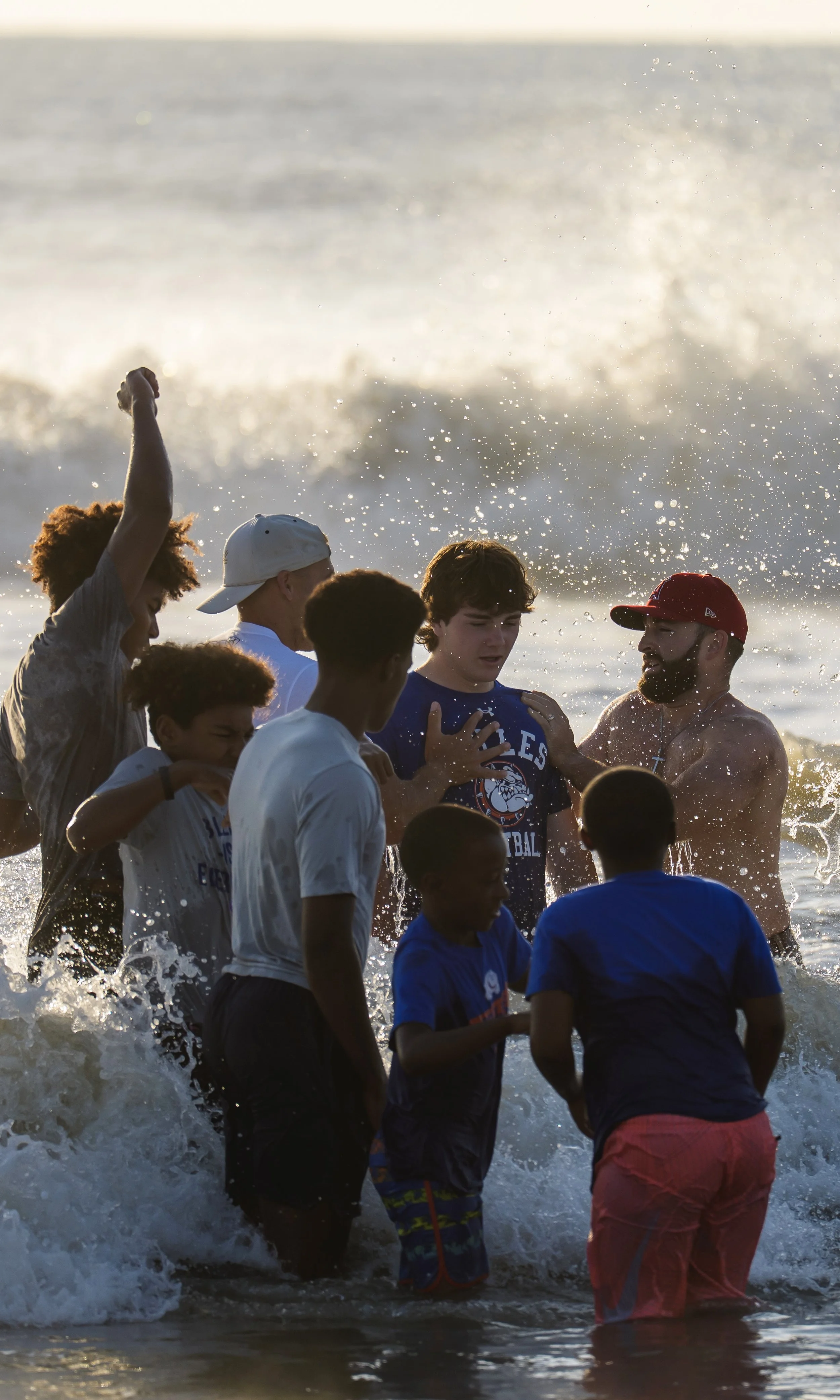 A group of children and a man are playing and splashing in the ocean near the shore during sunset or late afternoon.