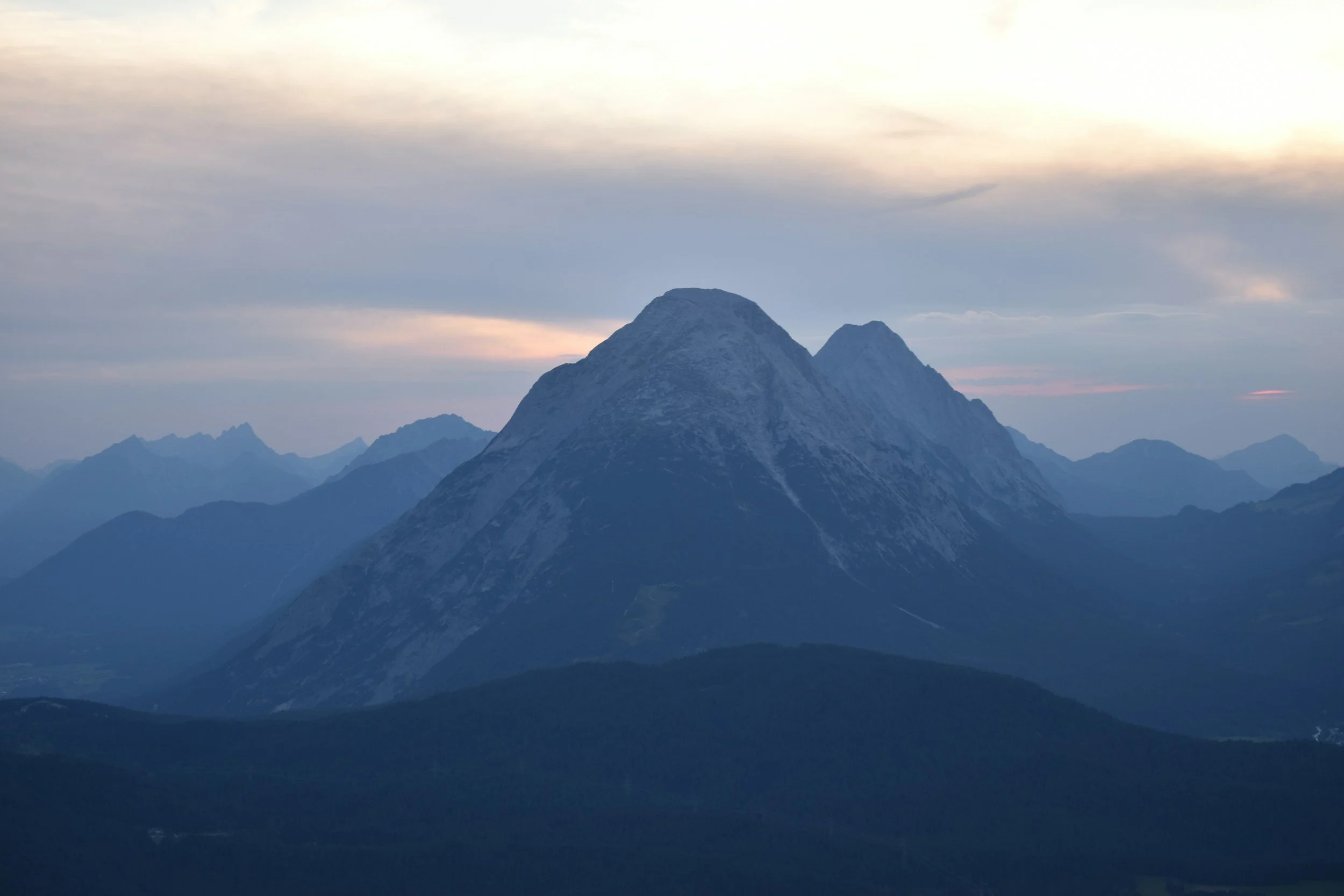 Mountain range with snow-capped peaks under a cloudy sky during dusk or dawn.