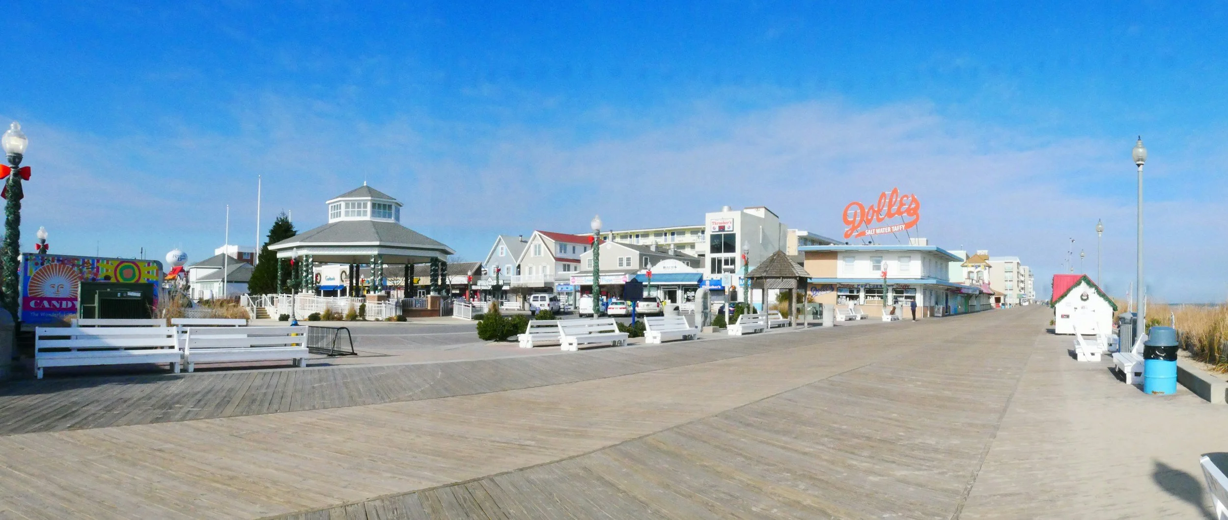 A seaside boardwalk town with benches, shops, and a large sign reading "Dolle's Salty Water Taffy" under a blue sky.