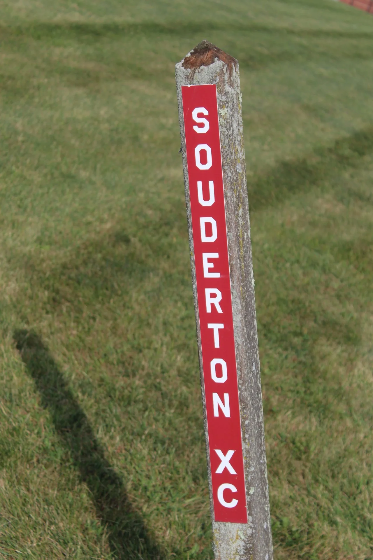 A weathered wooden post with a red and white sign that reads 'SOUTHERN X C' standing on a grassy field.