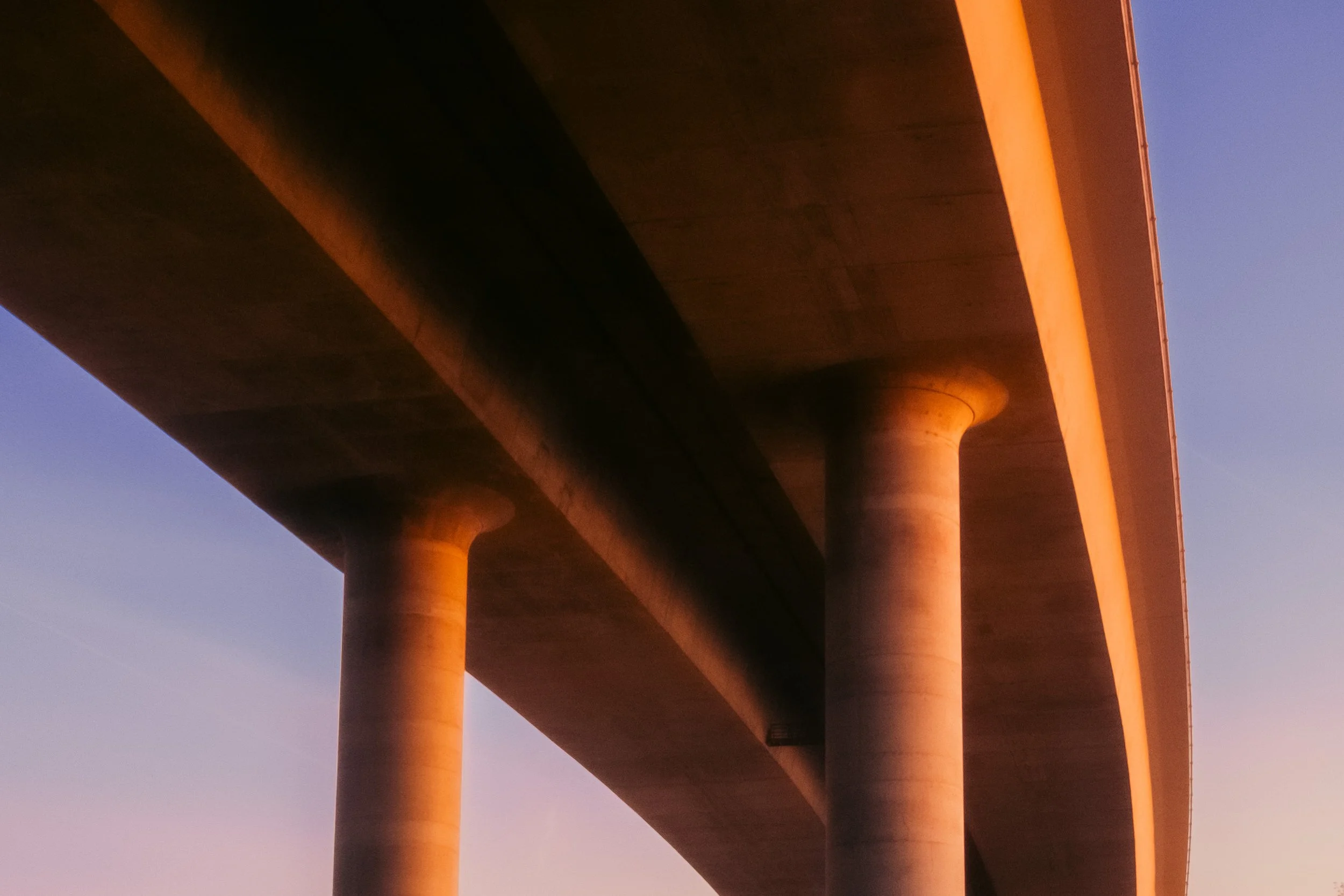 Cinematic, low-light photograph from "Sunset Blues" series by AJ Miranda, featuring a bloomy moon and silhouetted trees against a pink and orange Golden Hour skyscape.