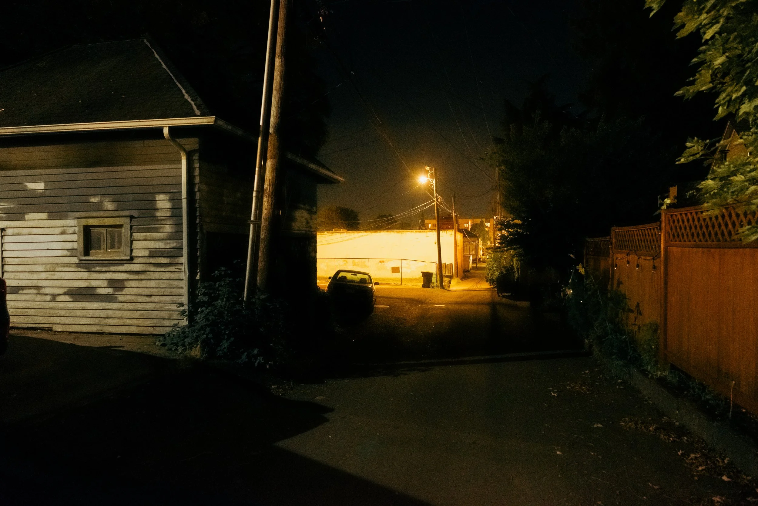 The Night By AJ Miranda Low-light, cinematic photograph of historic Vancouver, WA architecture during blue hour, using ambient light and deep chiaroscuro shadows to create an eerie film aesthetic.