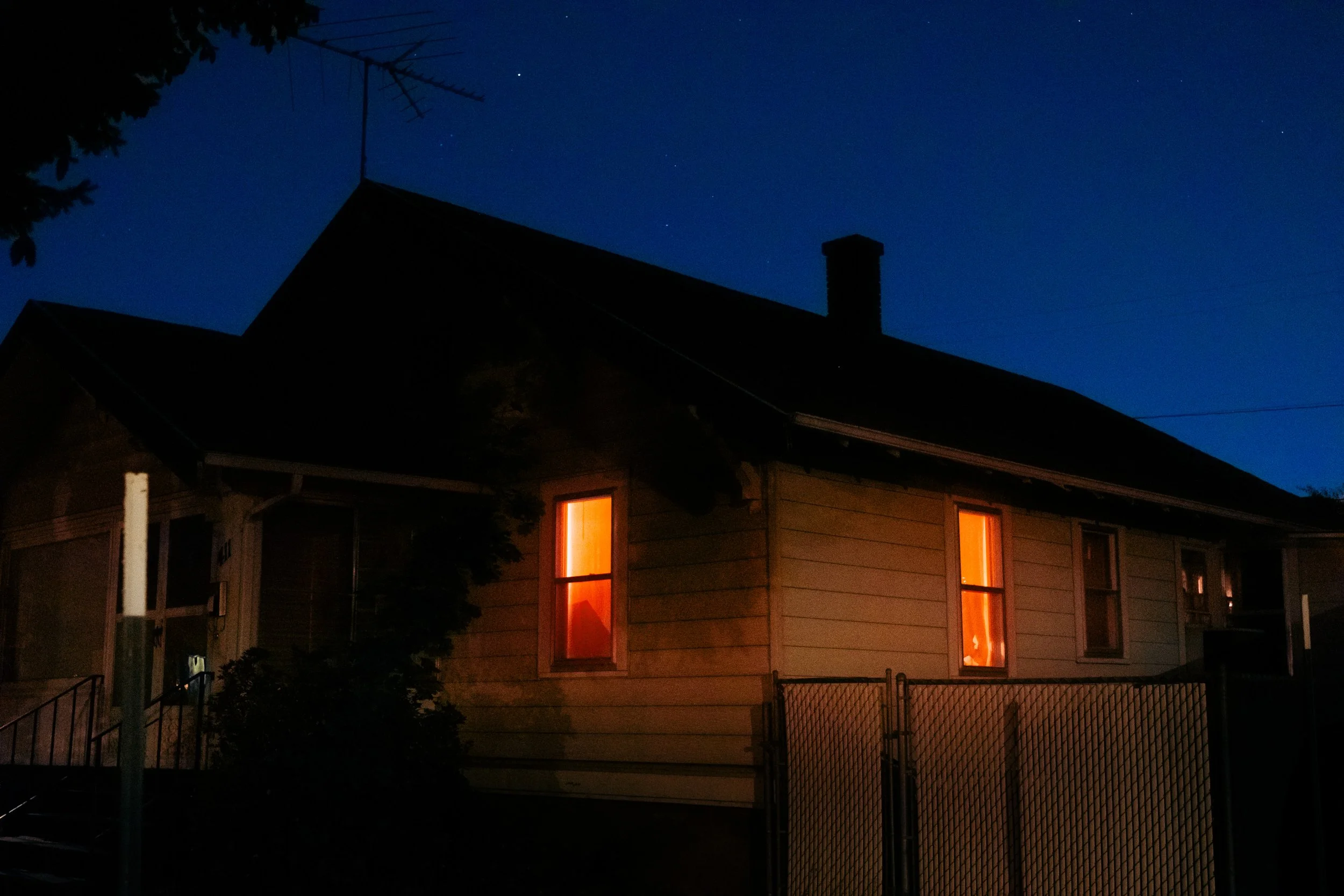 The Night By AJ Miranda Low-light, cinematic photograph of historic Vancouver, WA architecture during blue hour, using ambient light and deep chiaroscuro shadows to create an eerie film aesthetic.