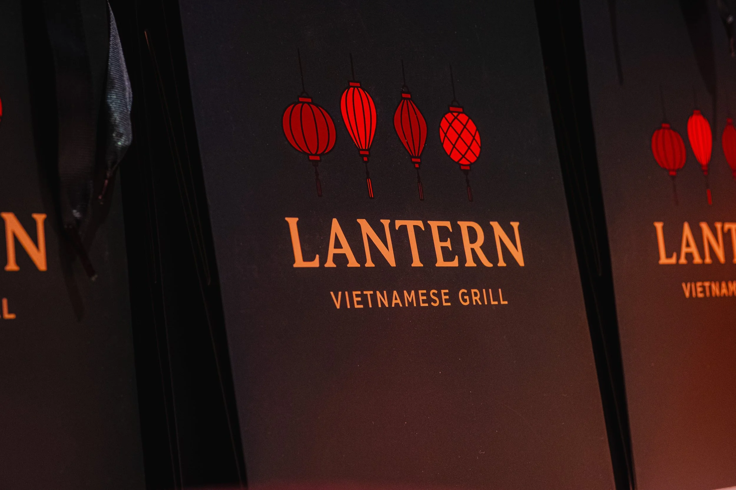 A menu cover for Lantern Vietnamese Grill with red lantern icons and gold lettering on a dark background.