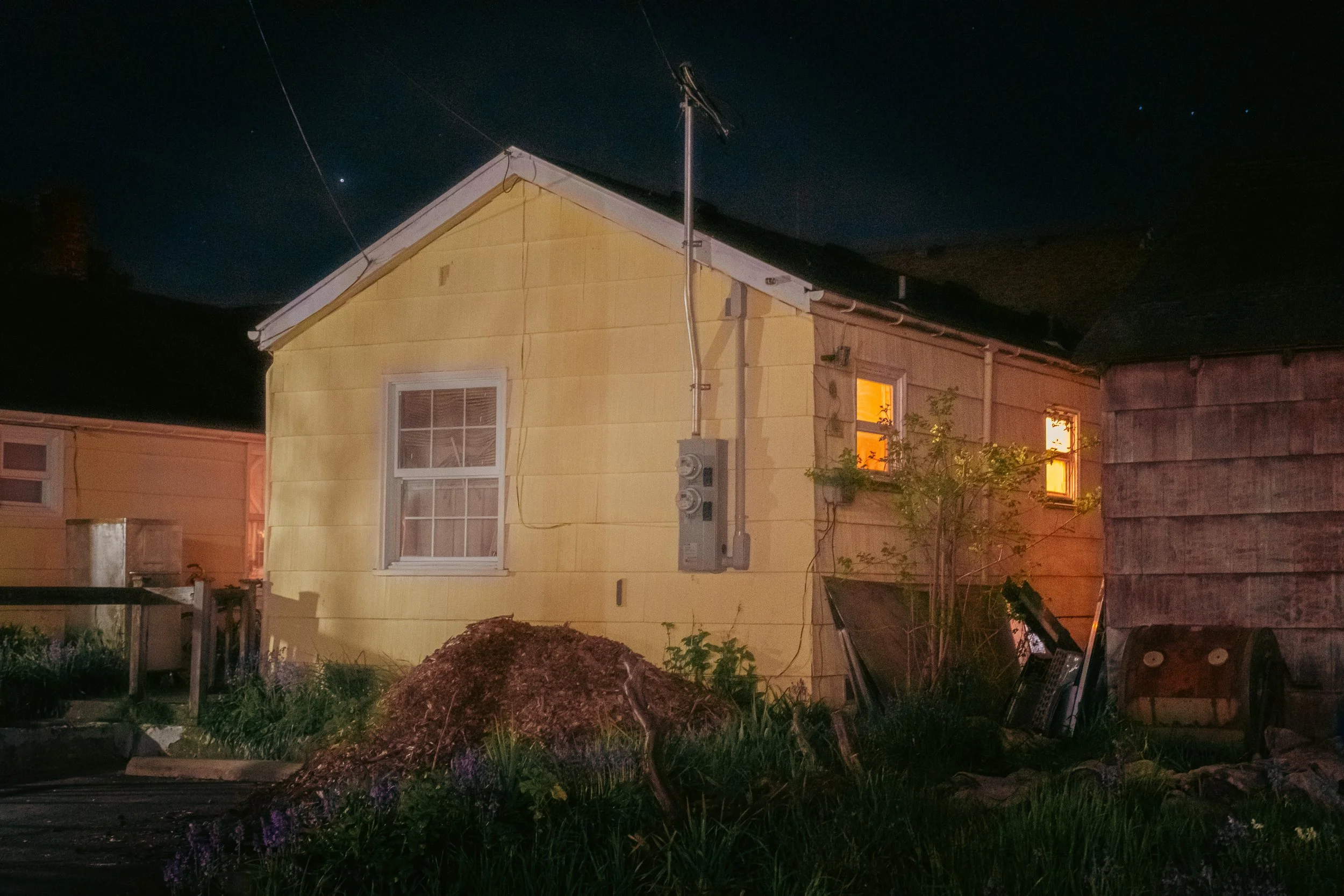 The Night By AJ Miranda Low-light, cinematic photograph of historic Vancouver, WA architecture during blue hour, using ambient light and deep chiaroscuro shadows to create an eerie film aesthetic.