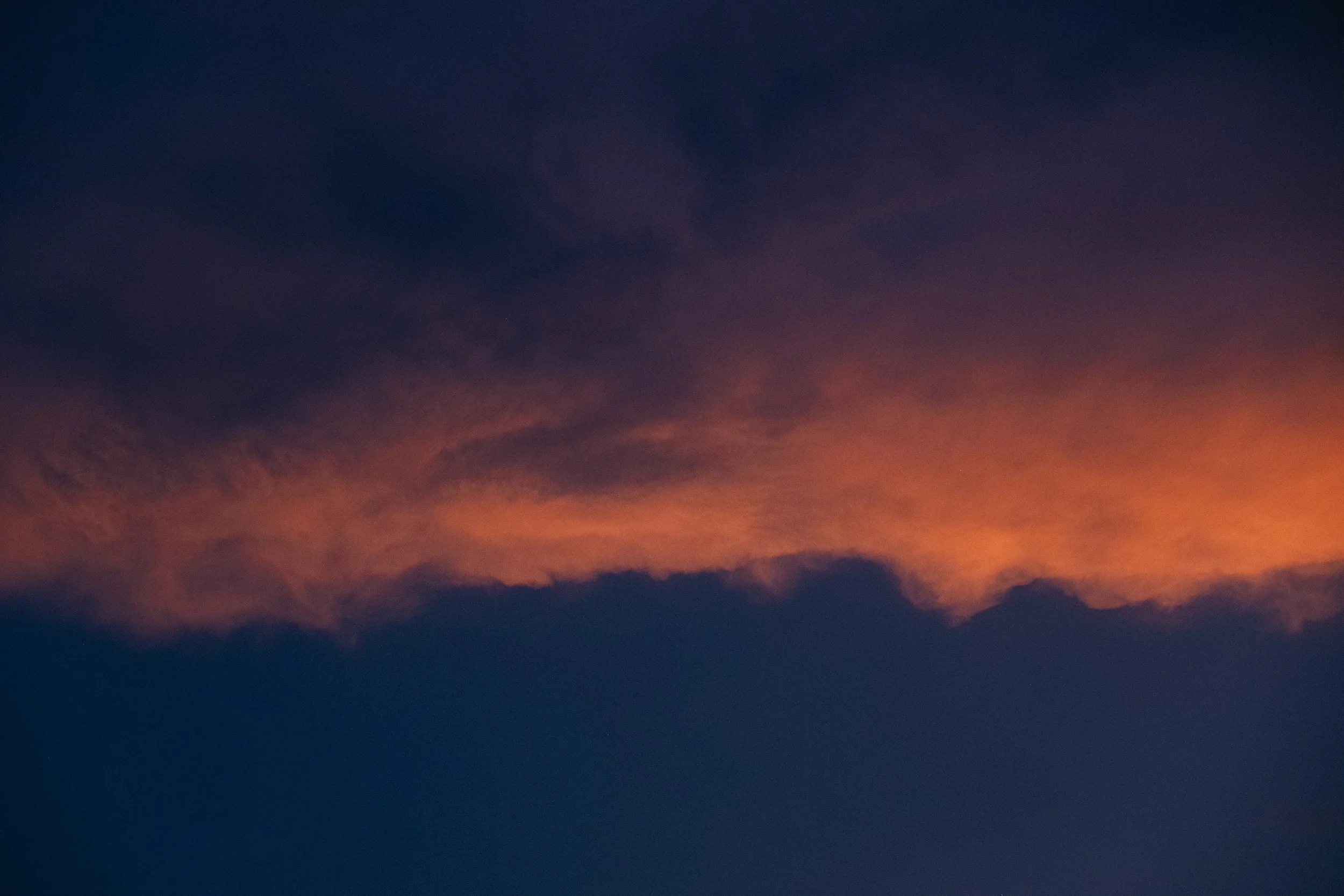 Cinematic, low-light photograph from "Sunset Blues" series by AJ Miranda, featuring a bloomy moon and silhouetted trees against a pink and orange Golden Hour skyscape.