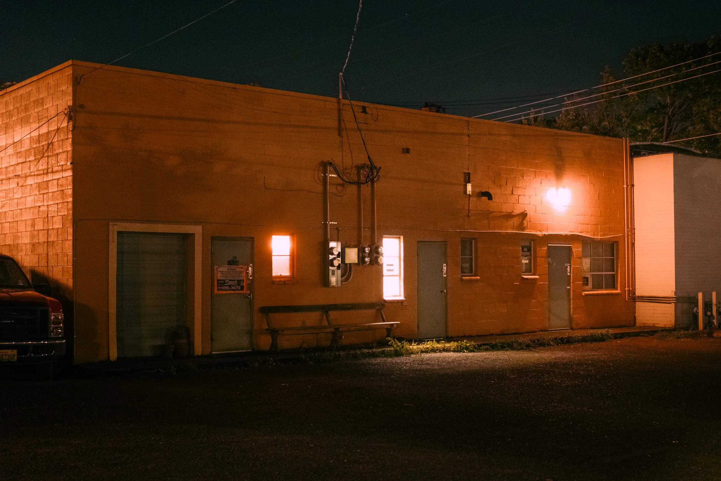 The Night By AJ Miranda Low-light, cinematic photograph of historic Vancouver, WA architecture during blue hour, using ambient light and deep chiaroscuro shadows to create an eerie film aesthetic.