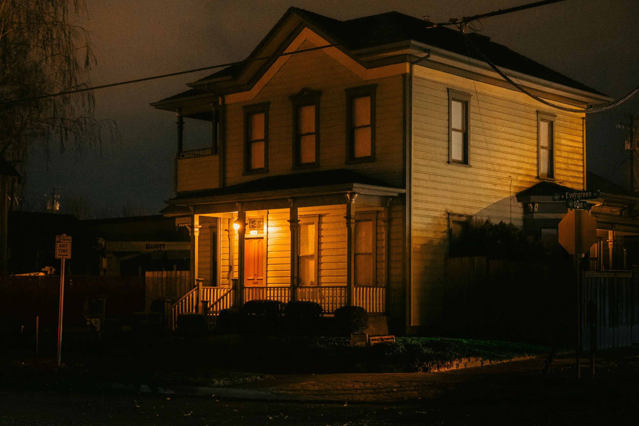 The Night By AJ Miranda Low-light, cinematic photograph of historic Vancouver, WA architecture during blue hour, using ambient light and deep chiaroscuro shadows to create an eerie film aesthetic.