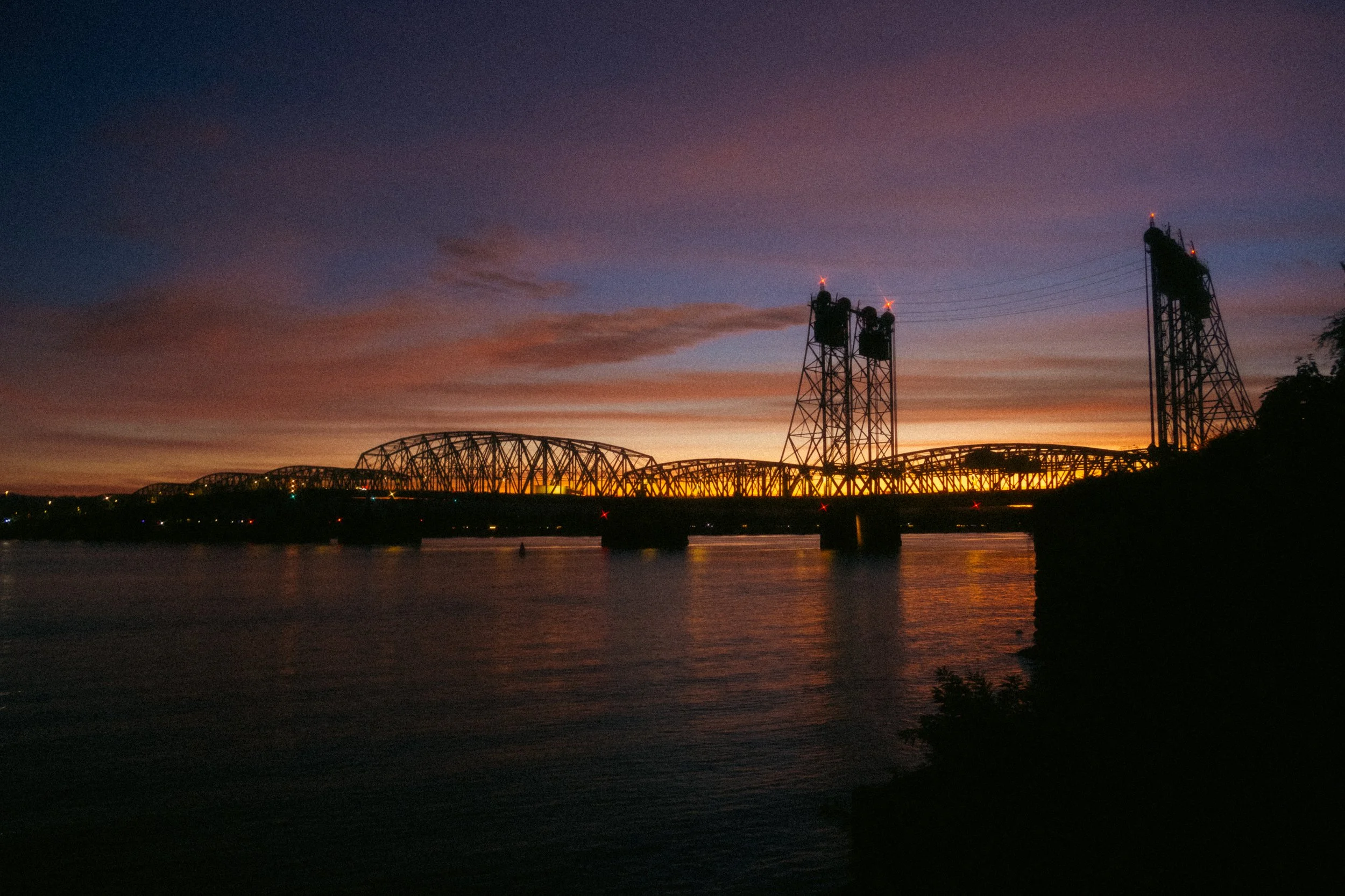 Cinematic, low-light photograph from "Sunset Blues" series by AJ Miranda, featuring a bloomy moon and silhouetted trees against a pink and orange Golden Hour skyscape.