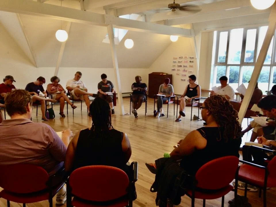 Evangeline Weiss Consulting | A group of people sitting in a circle in a brightly lit room with wooden floors and large windows, participating in a discussion or workshop.
