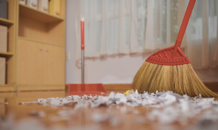 Evangeline Weiss Consulting | Broom sweeping paper scraps on a wooden floor near a window with curtains in a room.