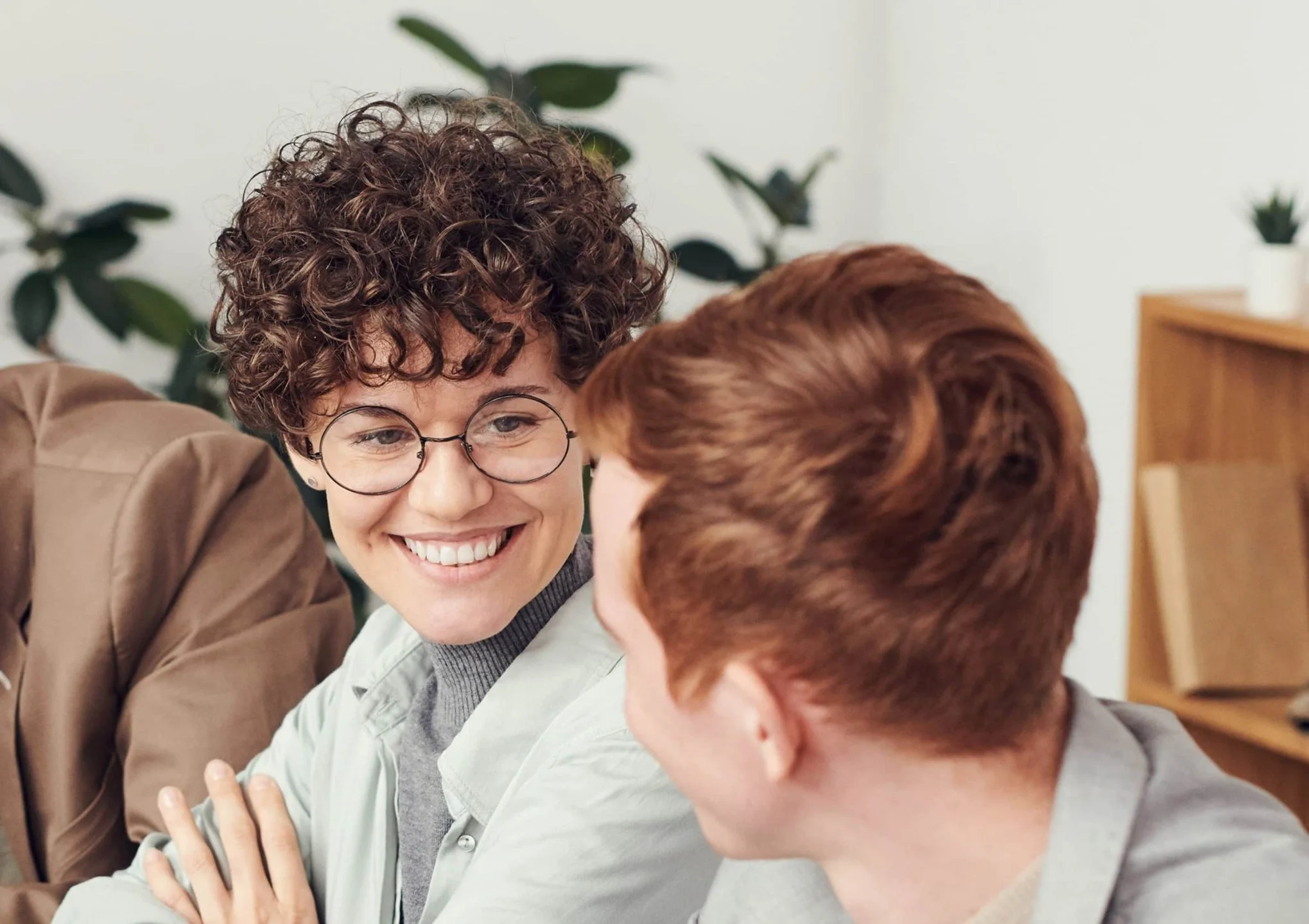 Evangeline Weiss Consulting | Two people smiling and engaging in conversation indoors with houseplants in the background.