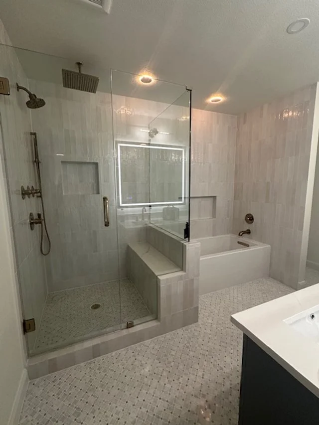 Bathroom with a glass-enclosed shower, a bathtub, and a vanity with a white sink.