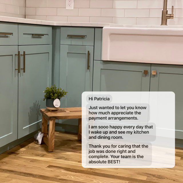 Kitchen with light teal cabinets, white subway tile backsplash, wooden floor, small wooden bench, potted plant, and a white farmhouse sink with a gold faucet.