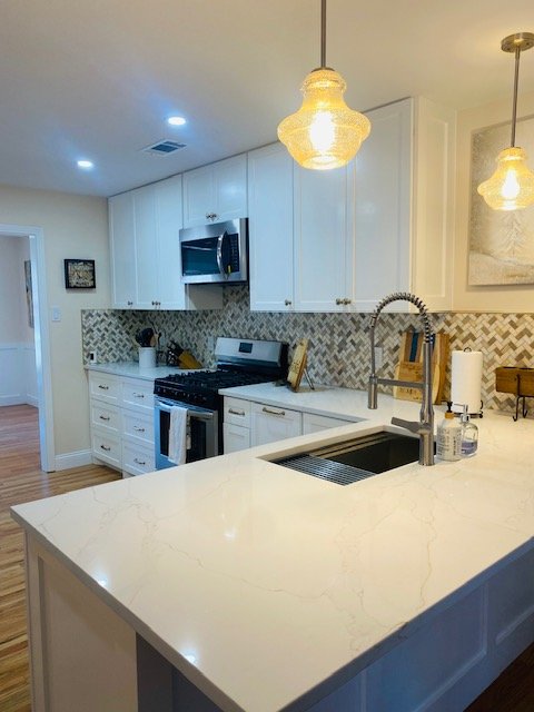 Modern kitchen with white cabinets, marble countertop, stainless steel sink, and a chevron tile backsplash