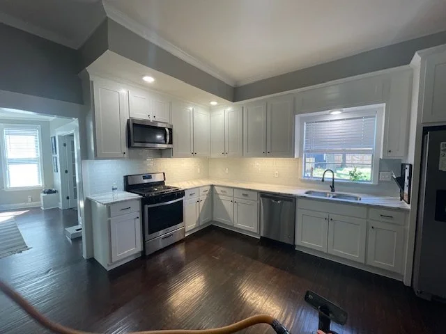 Modern kitchen with white cabinetry, stainless steel appliances, dark hardwood floors, and a window over the sink.