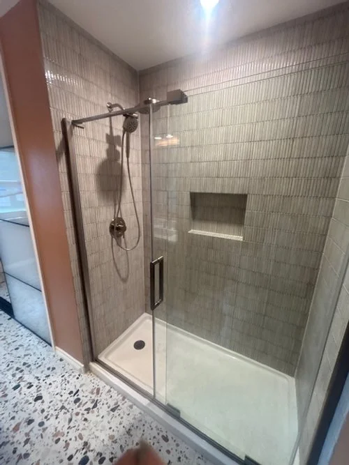 Modern walk-in shower with glass door, tiled walls, built-in niche, showerhead, and handheld shower apparatus.